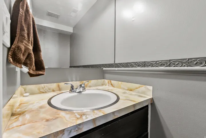 Bathroom vanity featuring an oval undermount sink with chrome fixtures, a light-toned marble-look countertop, and a decorative wall trim