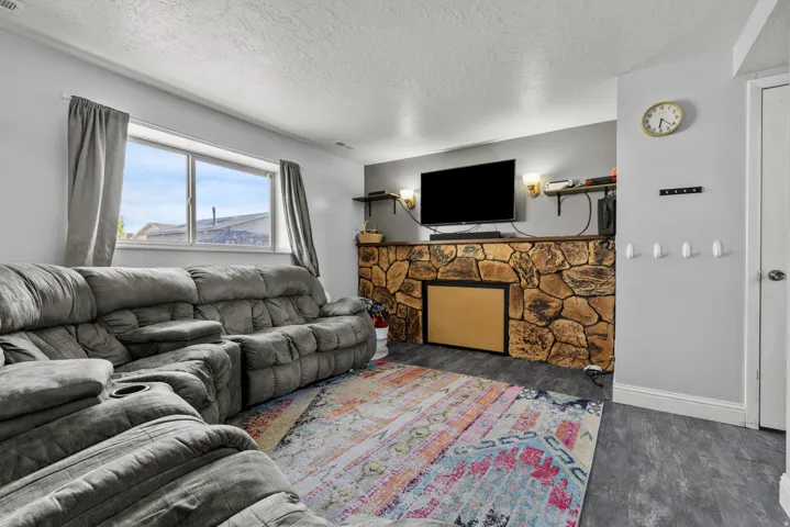 Living area featuring a stone-clad fireplace surround, a window offering natural light, and dark wood-finish flooring