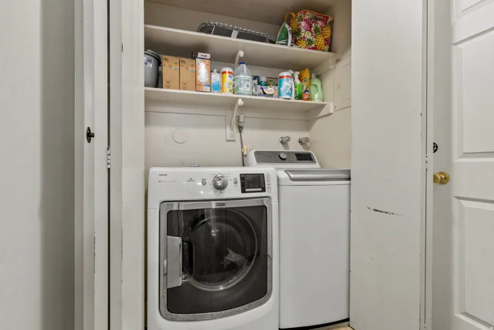 Dedicated laundry closet featuring a front-loading washer, a top-loading dryer, and overhead shelving for storage