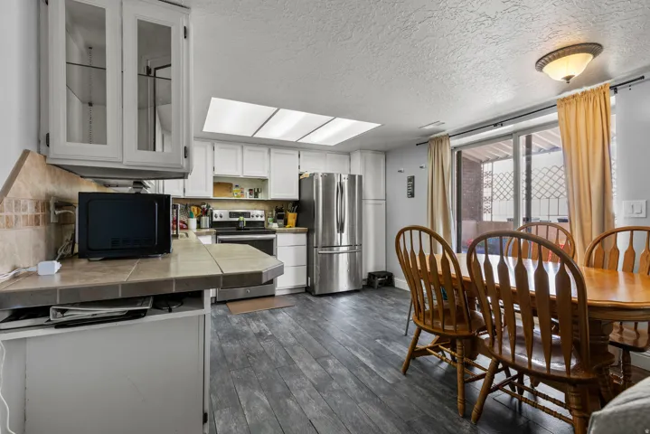 Kitchen and dining area featuring wood-finish flooring, white cabinetry, integrated stainless steel appliances, and a skylight
