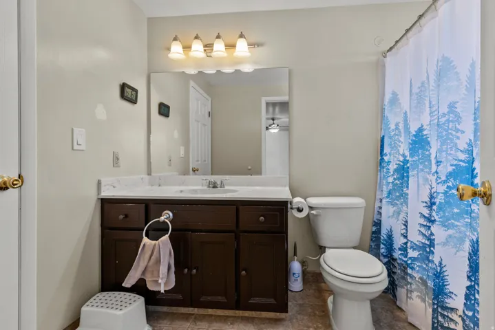 Bathroom featuring a dark wood vanity with a white countertop and integrated sink, a wall-mounted mirror, overhead lighting, and a white toilet