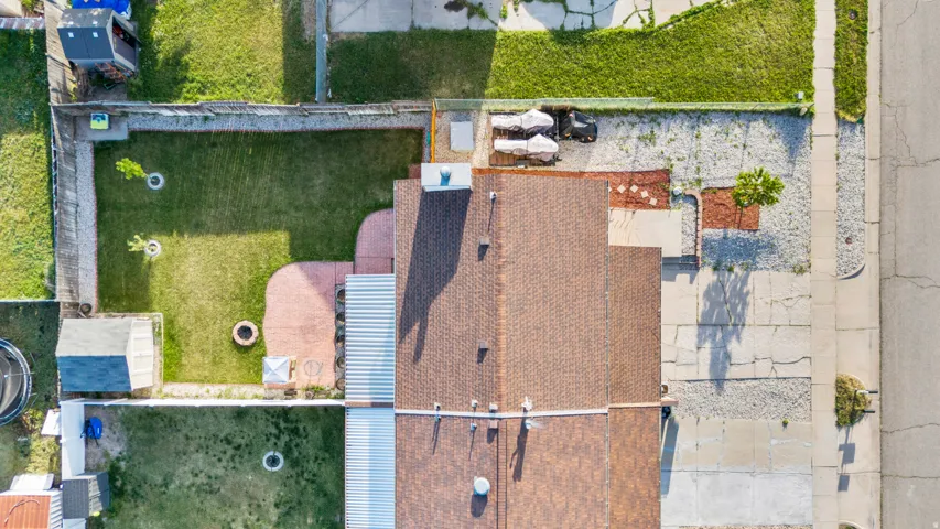 Property featuring a brown shingle roof, a backyard with a manicured lawn, a fire pit, and an attached paved patio