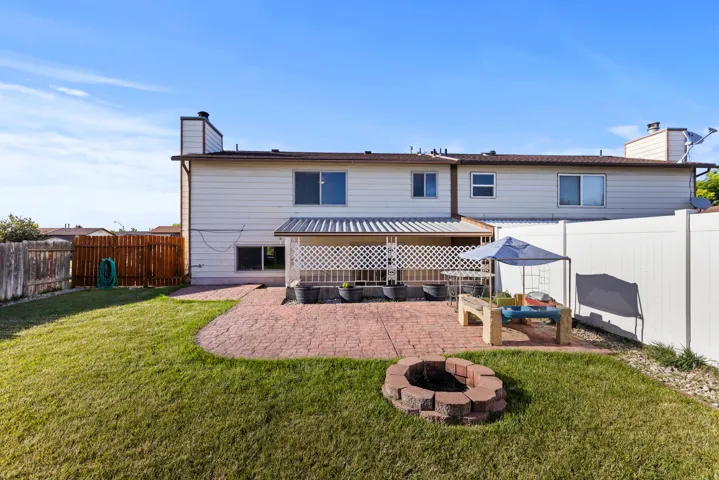 Expansive backyard featuring a patterned paver patio, a built-in fire pit, a covered porch, and a combination of wood and vinyl fencing