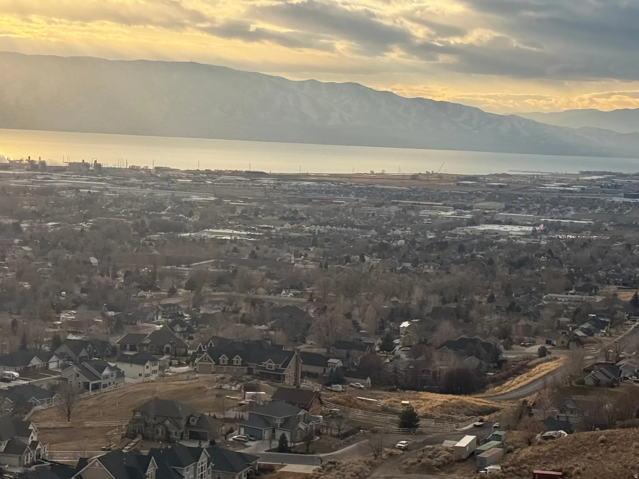 Expansive elevated landscape featuring a distant body of water, snow-capped mountains, and a sprawling residential area
