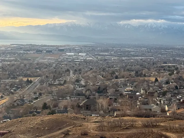 Expansive regional panorama featuring distant snow-capped mountains, a large body of water, and a widespread residential landscape