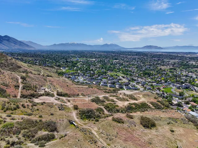 Expansive hillside property featuring undeveloped terrain with distant residential areas, mountains, and a large body of water under a clear blue sky