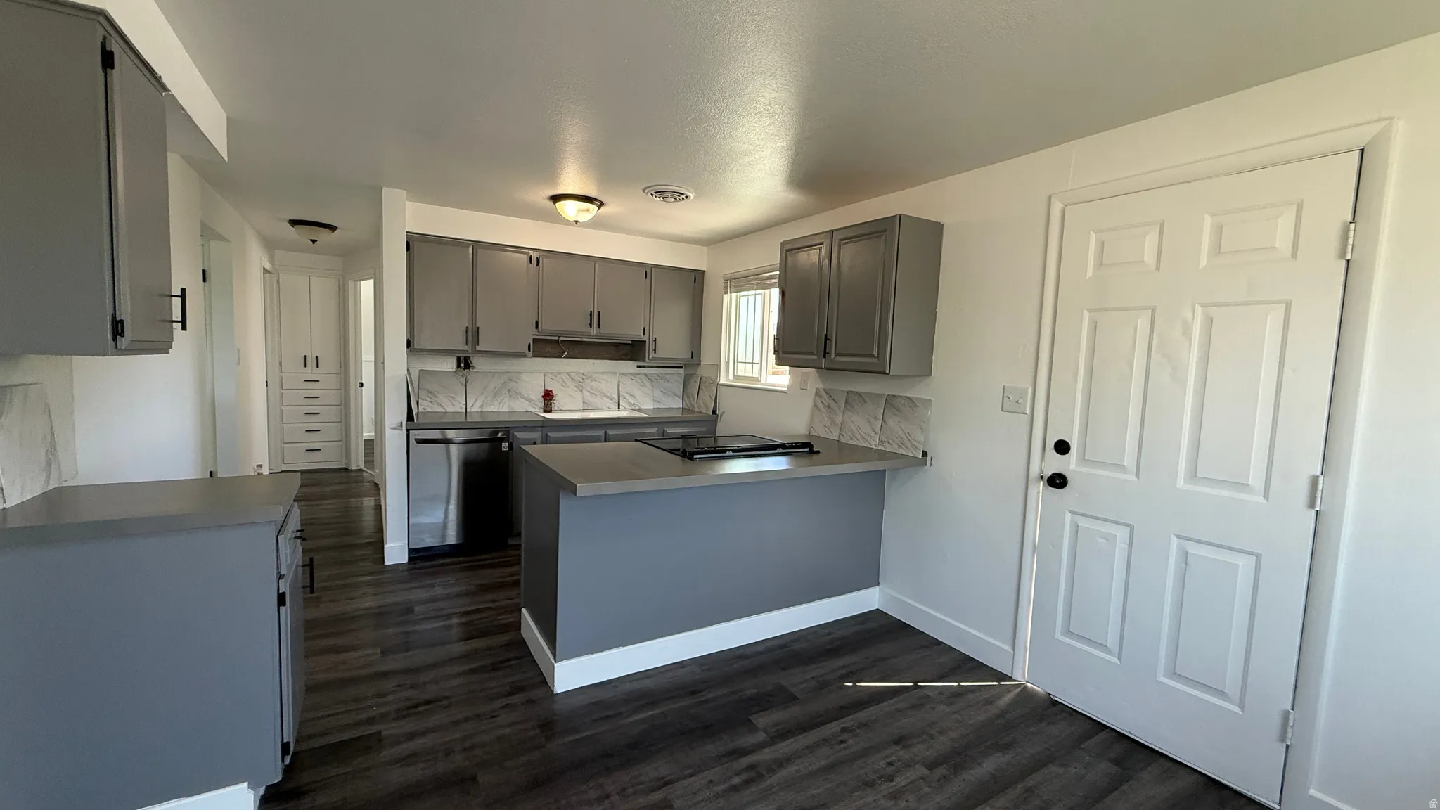 Kitchen featuring grey cabinetry, stainless steel dishwasher, an island with countertop space, patterned tile backsplash, and dark wood-finish flooring