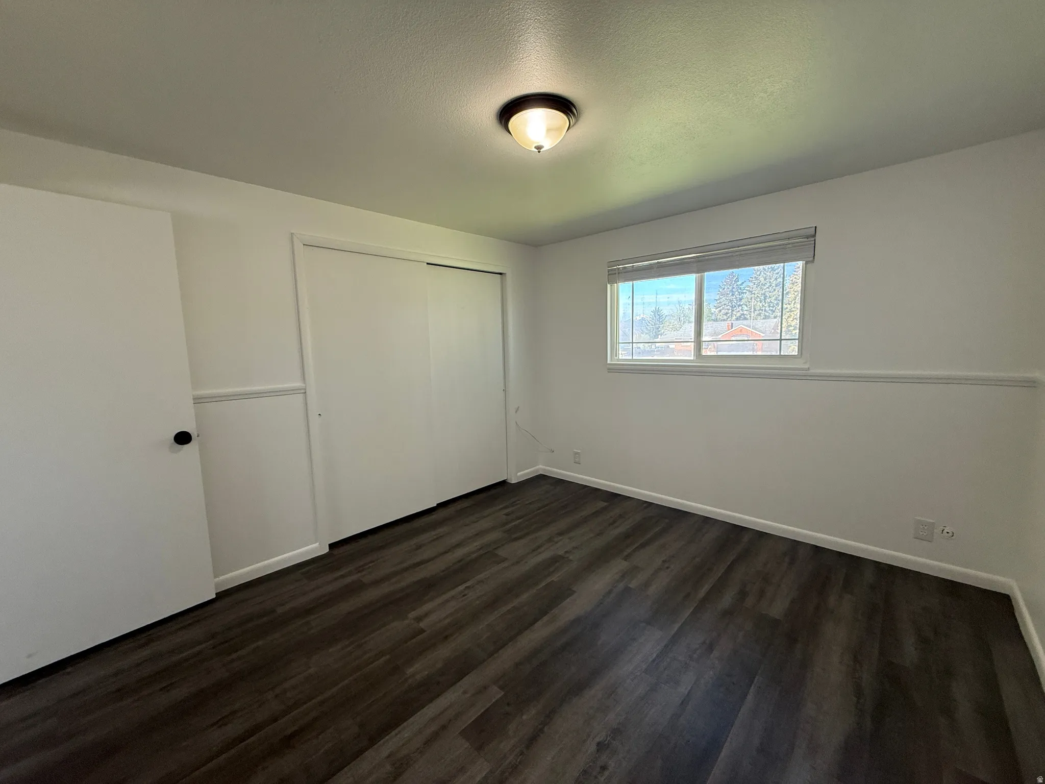 Bright room featuring dark wood-finish flooring, white walls, and a recessed window with blinds