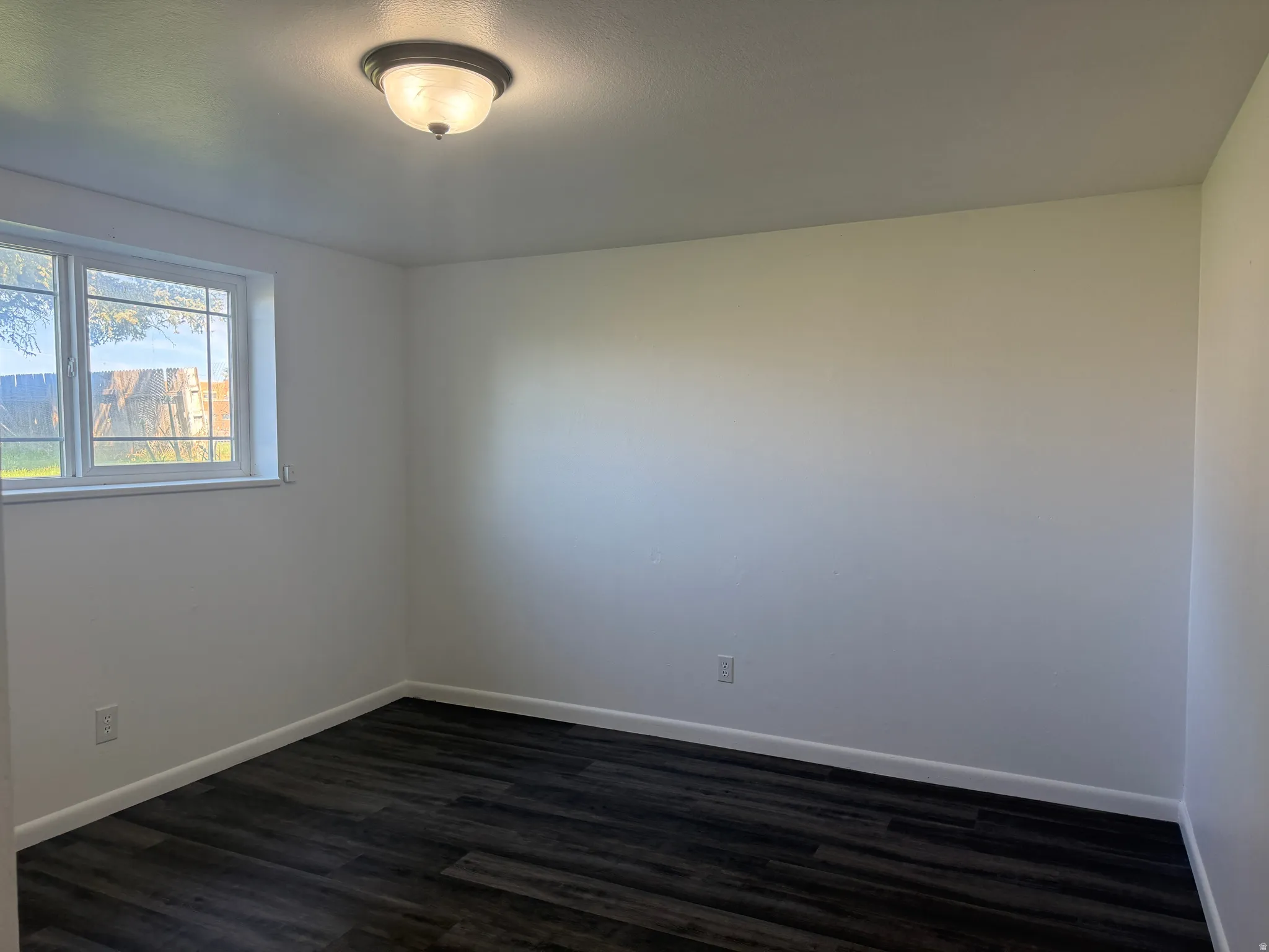 Room featuring dark wood-finish flooring, white baseboards, a single window, and a flush-mount ceiling light fixture