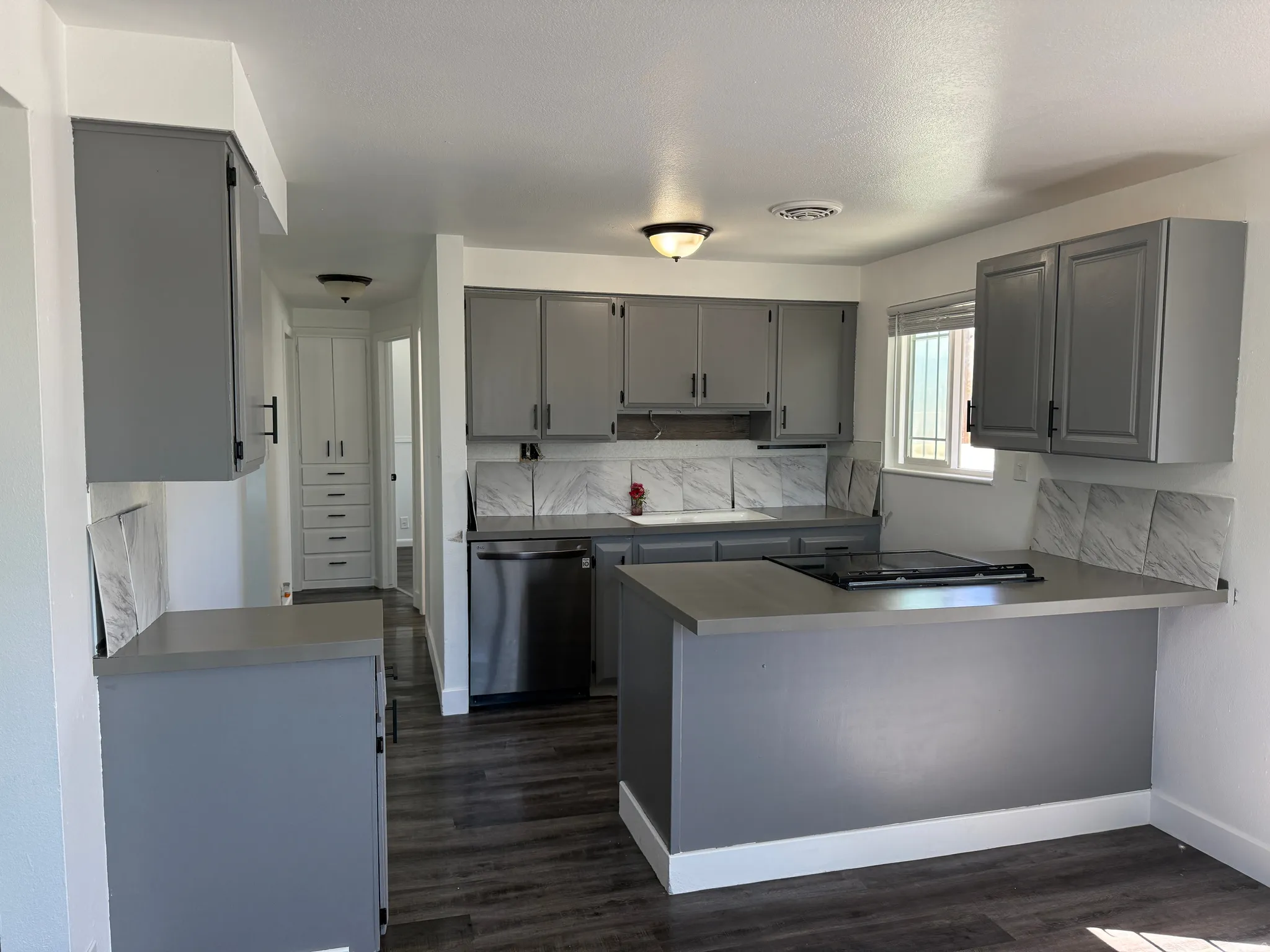 Modern kitchen featuring grey cabinetry, stainless steel dishwasher, and a built-in cooktop on a peninsula with bar seating