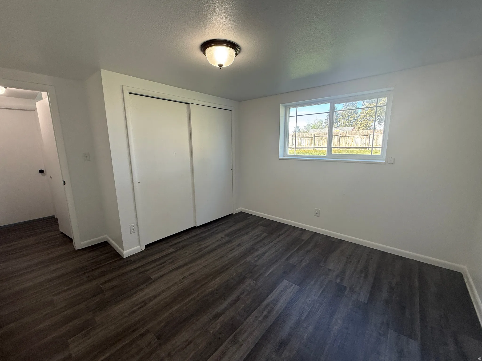 Interior room featuring dark wood-finish flooring, light-colored walls, and a window providing natural illumination