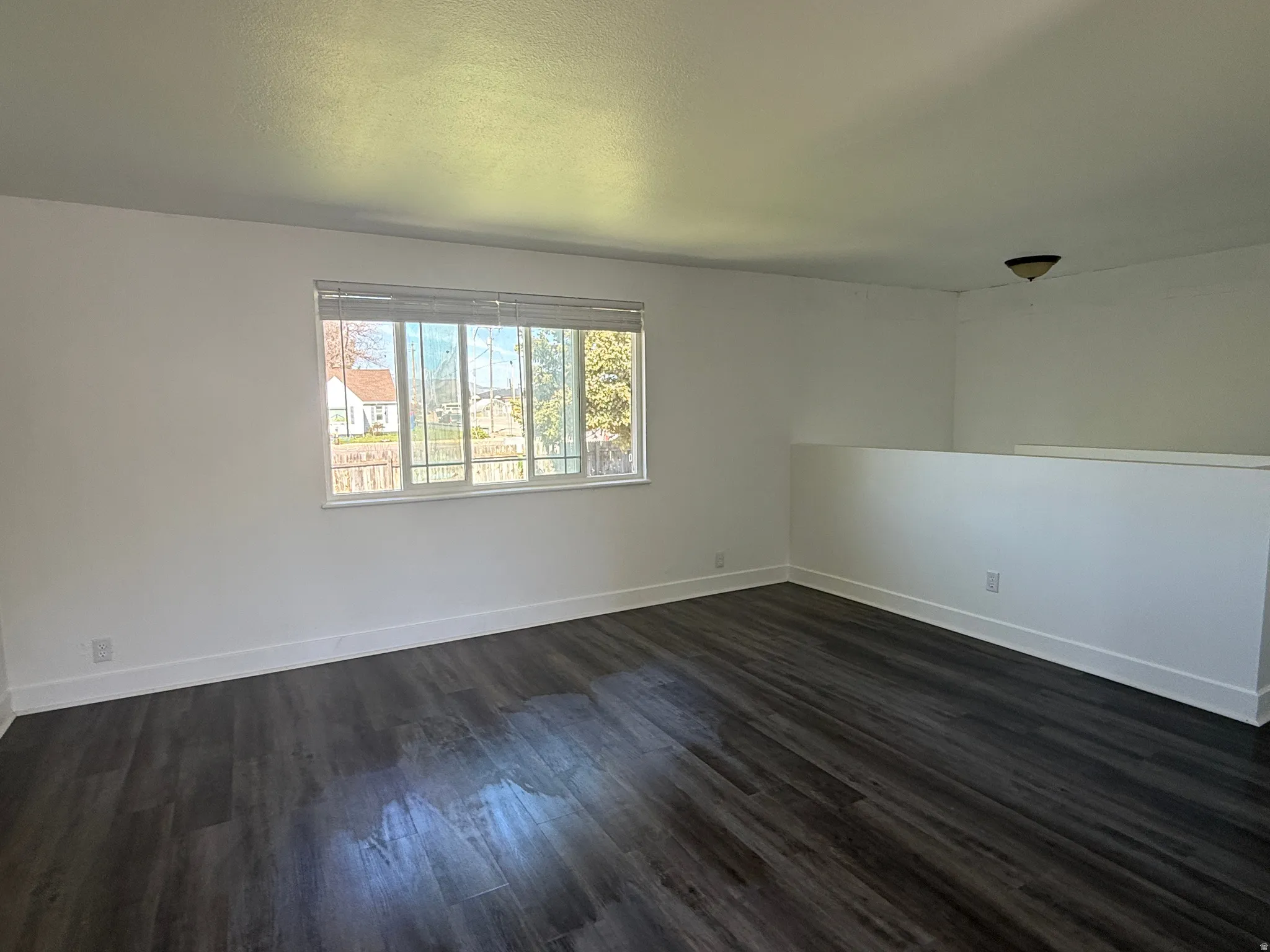 Open-concept room featuring wood-finish flooring, a contemporary window, and a partial wall structure