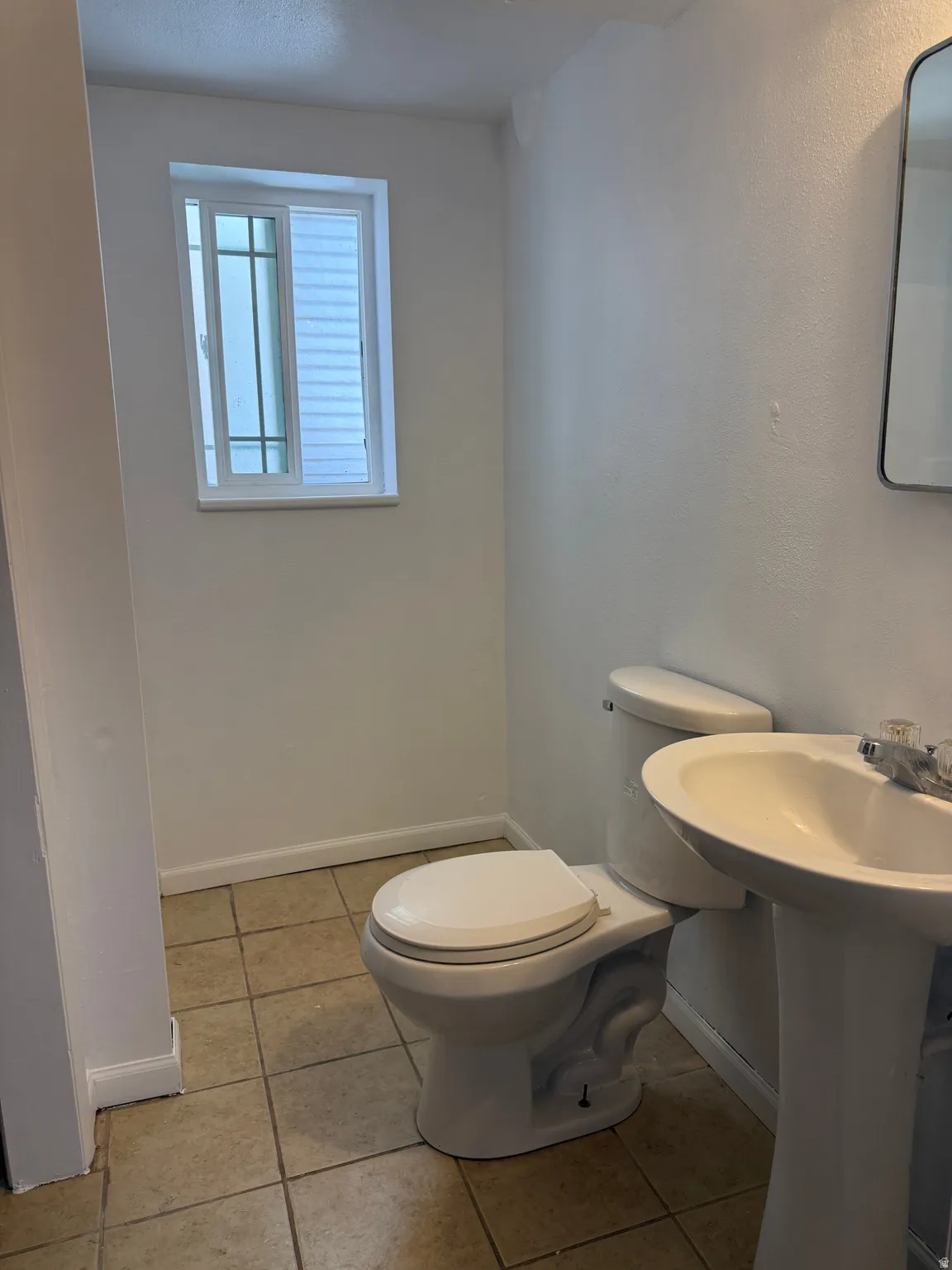 Bathroom featuring a white pedestal sink, toilet, and a window with horizontal grilles