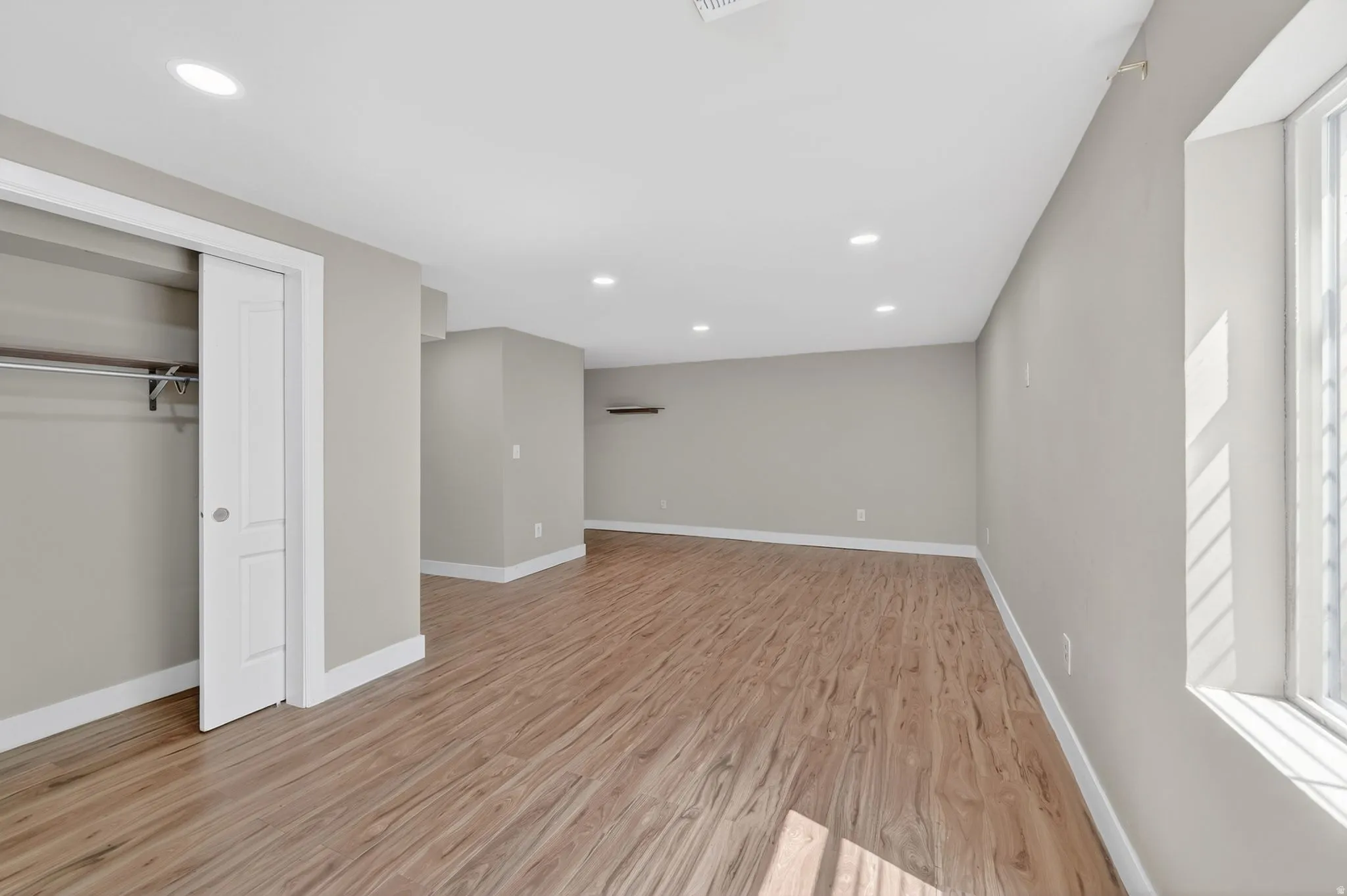 Spacious room featuring wood-finish flooring, recessed lighting, neutral wall tones, and a built-in closet with sliding doors