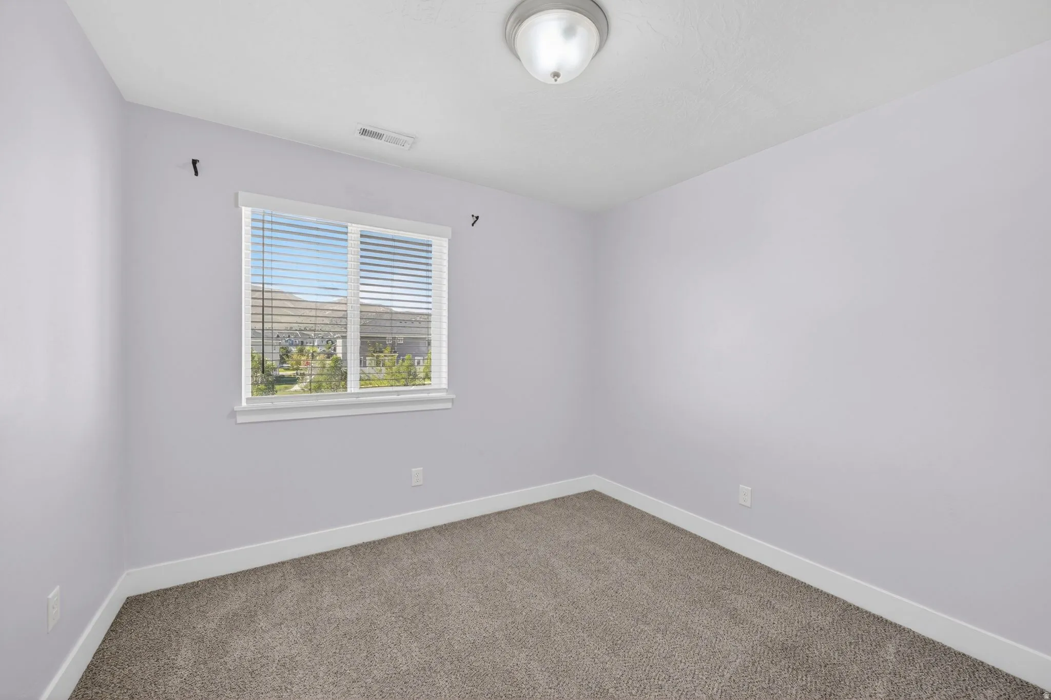 Interior room featuring light-colored walls, carpet flooring, a window with blinds, and a flush-mount ceiling light fixture