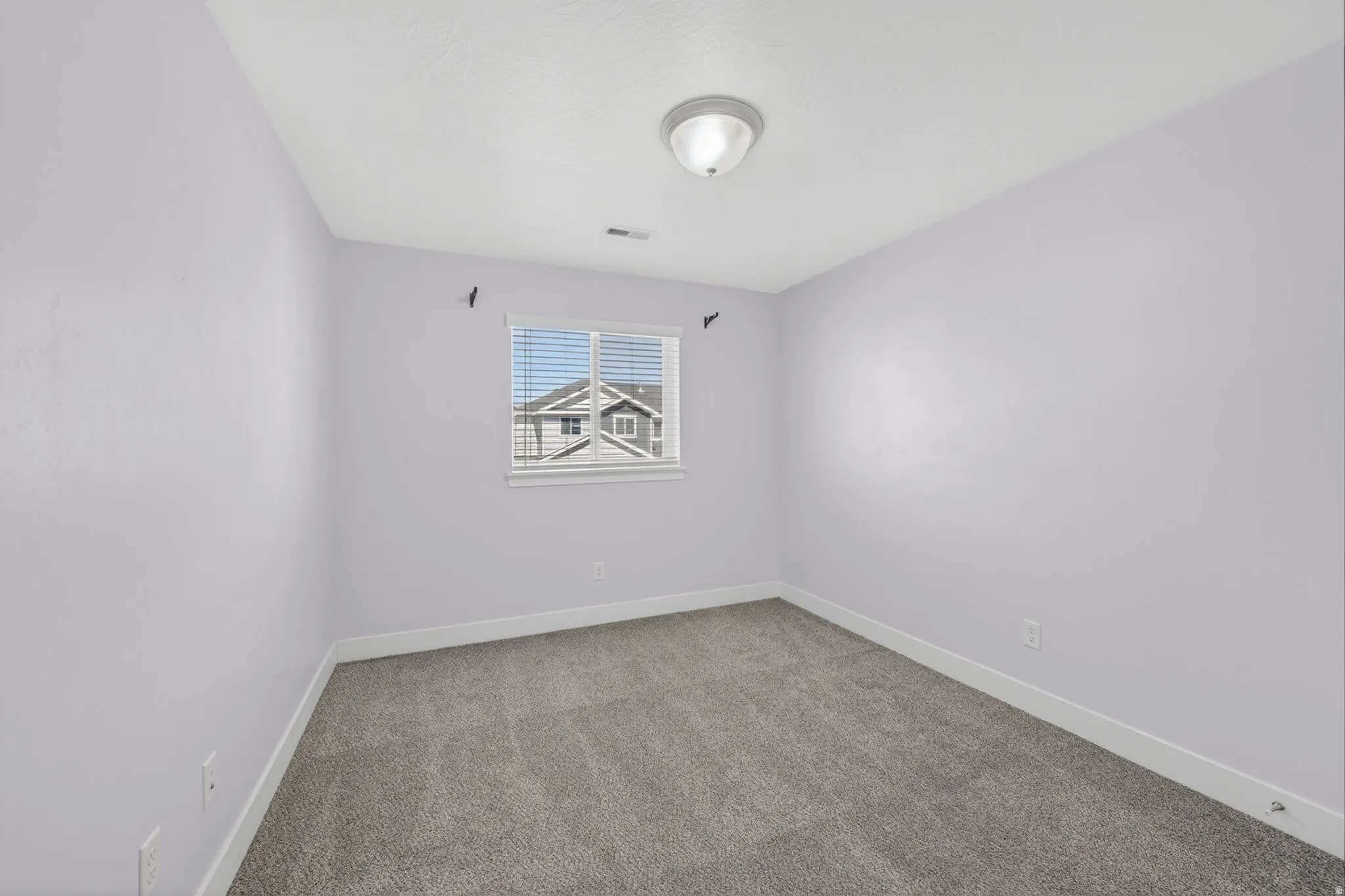 Room with light-colored walls, gray carpet flooring, and a single window with blinds