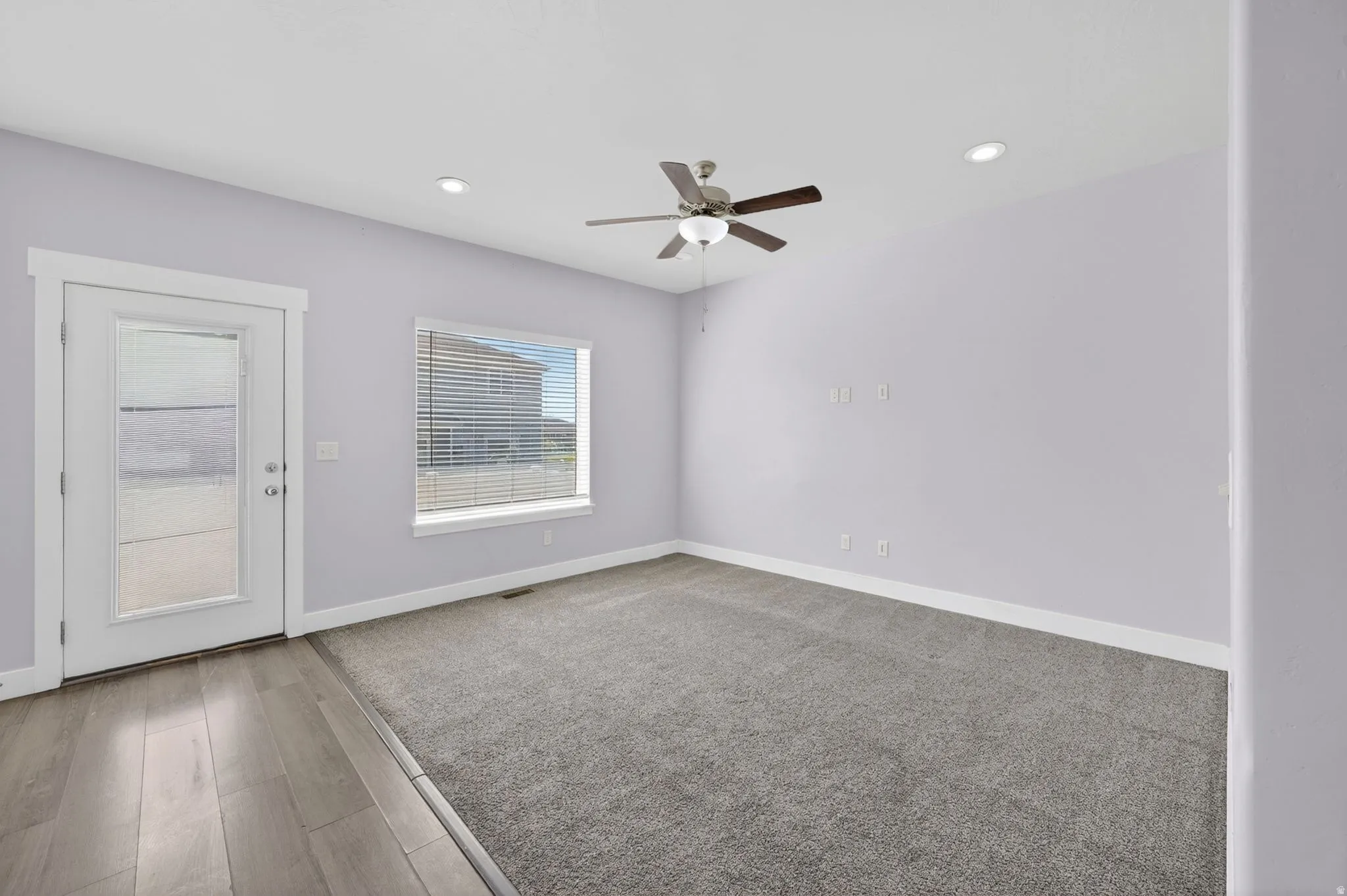 Spacious room featuring light gray walls, recessed lighting, a ceiling fan with light fixture, a window with horizontal blinds, and a glass-paneled door