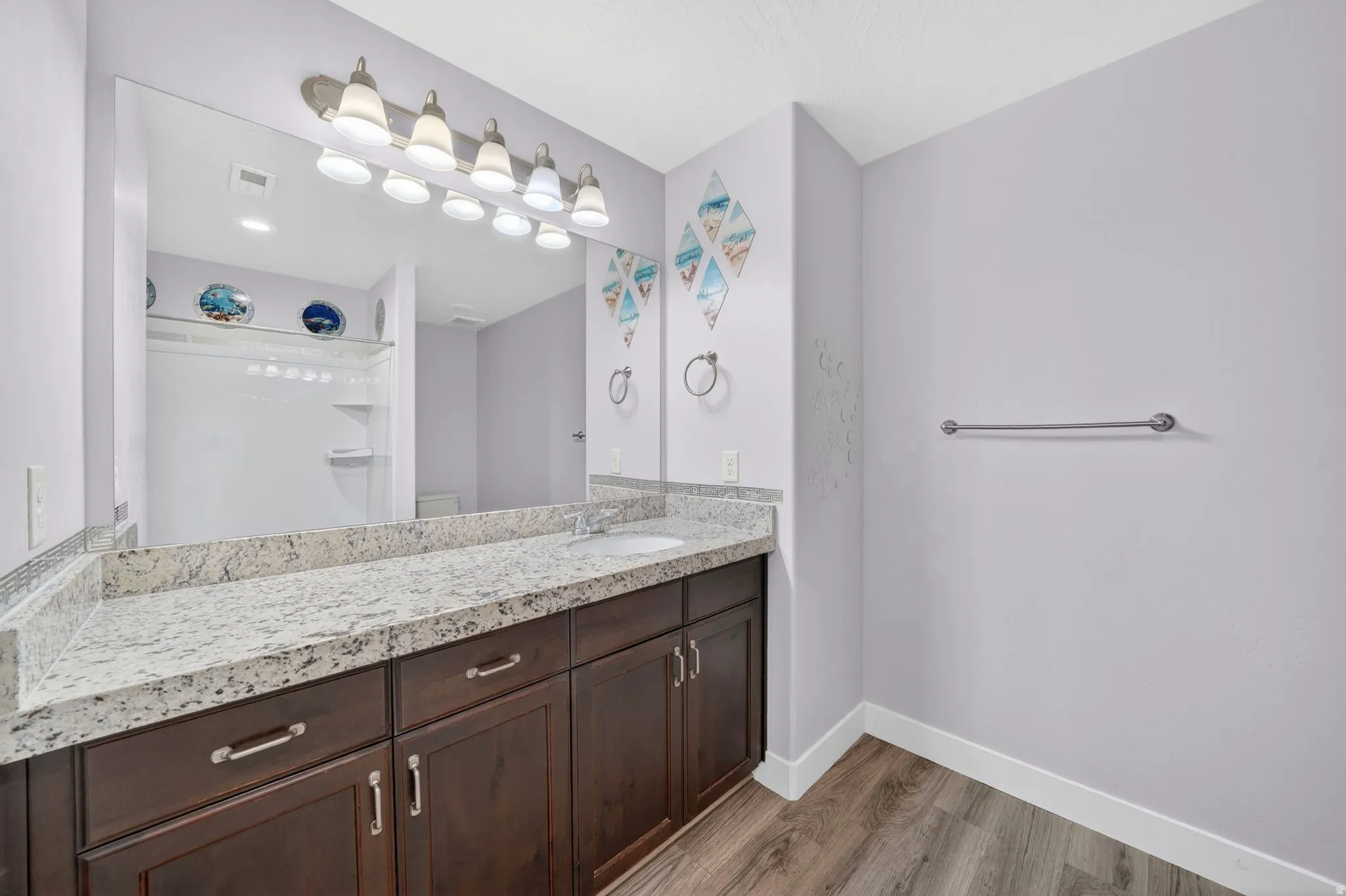 Bathroom featuring a lengthy dark wood-finish vanity with a light speckled countertop and a full-width mirror