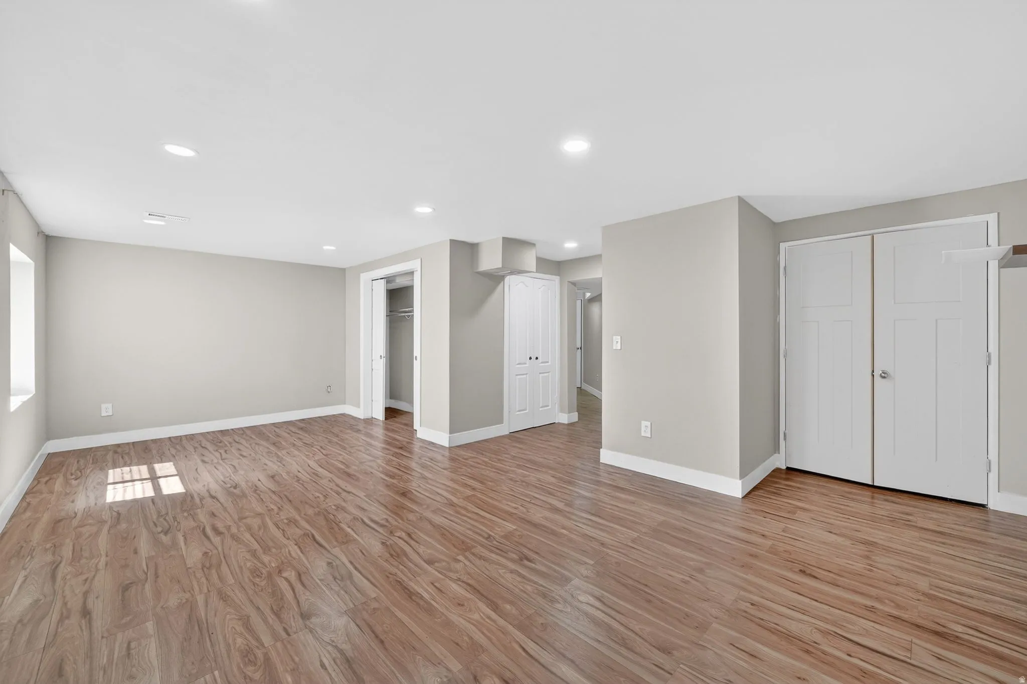 Spacious room featuring wood-finish flooring, recessed lighting, neutral paint, multiple white bi-fold closet doors, and a window