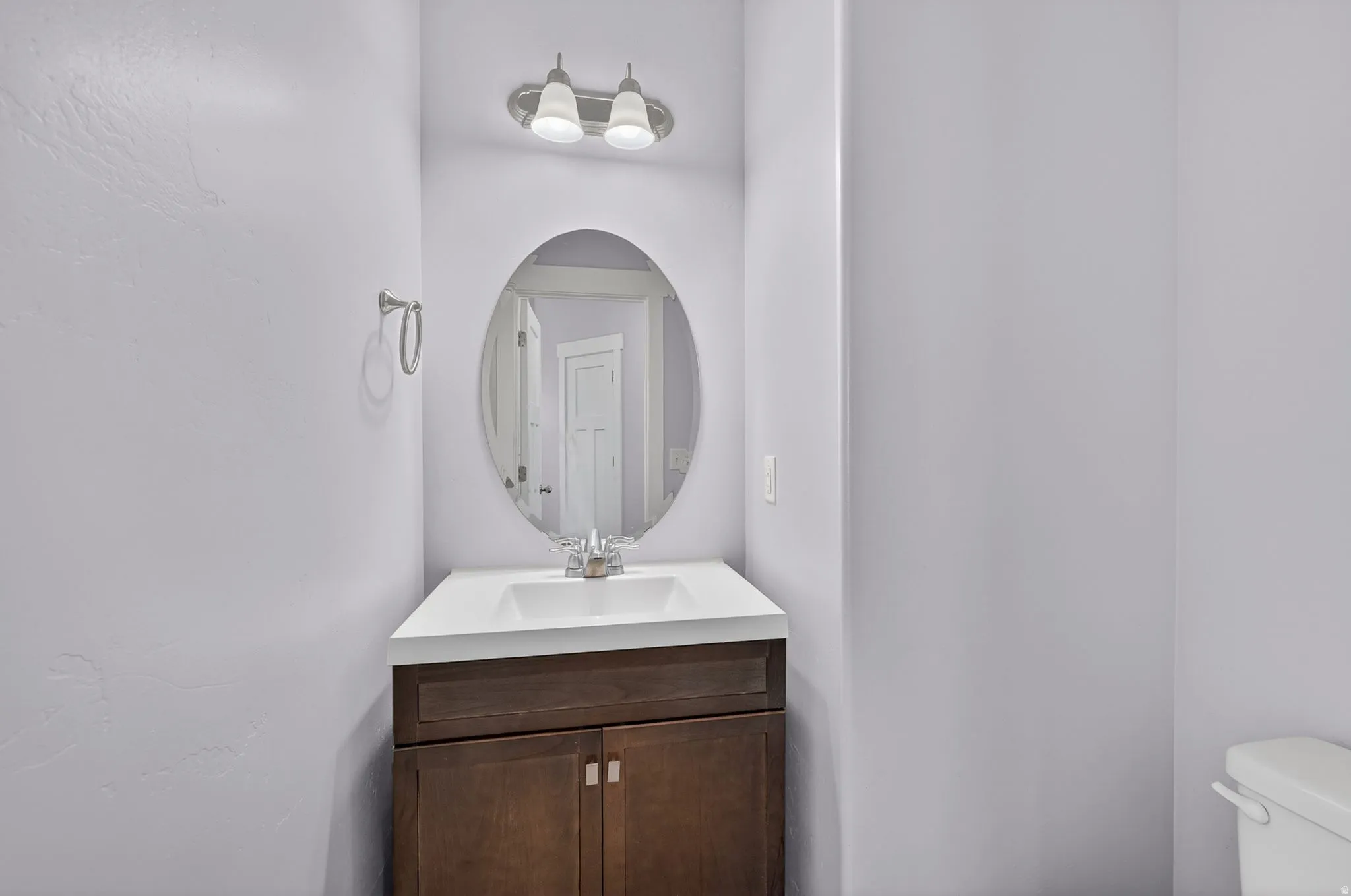 Vanity featuring an oval mirror, two-light fixture, white countertop, and dark wood-finish cabinetry