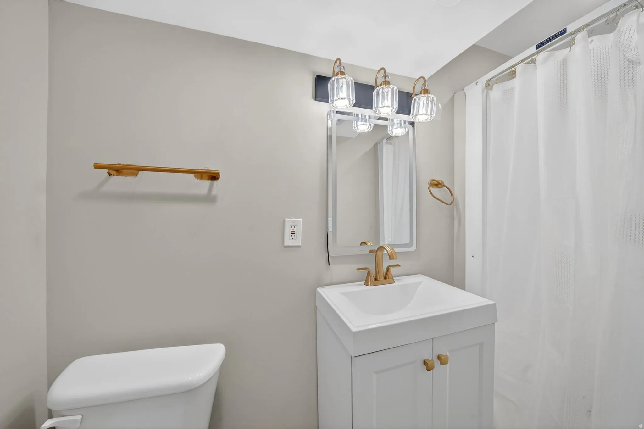 Bathroom featuring a white vanity with a single basin sink, gold-finish faucet, and coordinating gold-finish hardware