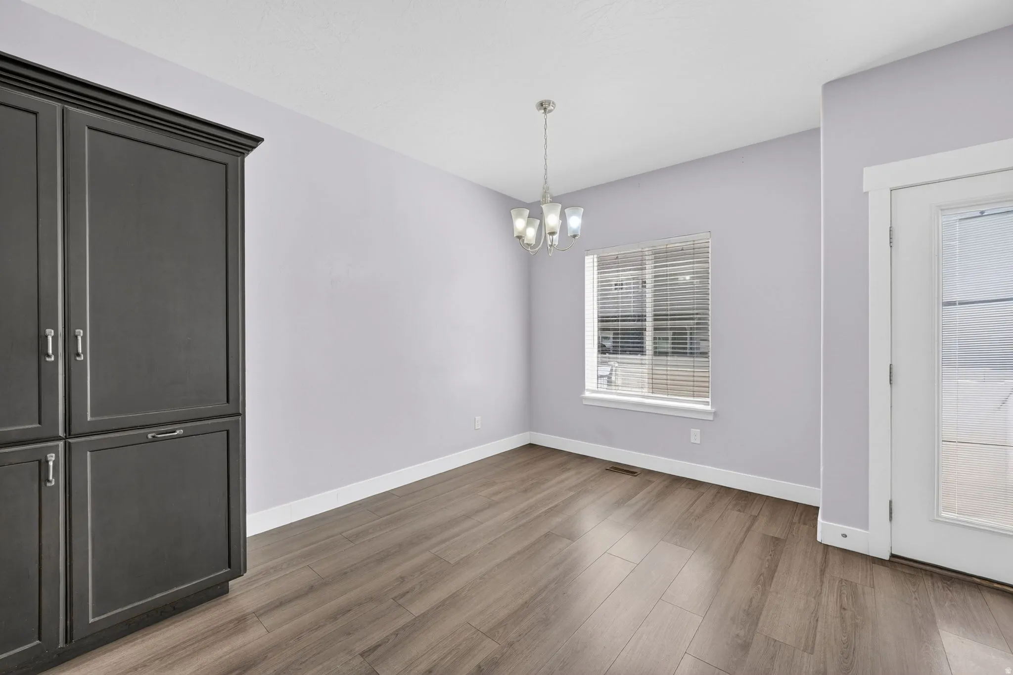 Dining area with dark wood-finish built-in cabinetry, wood-finish flooring, a window with blinds, and an overhead chandelier
