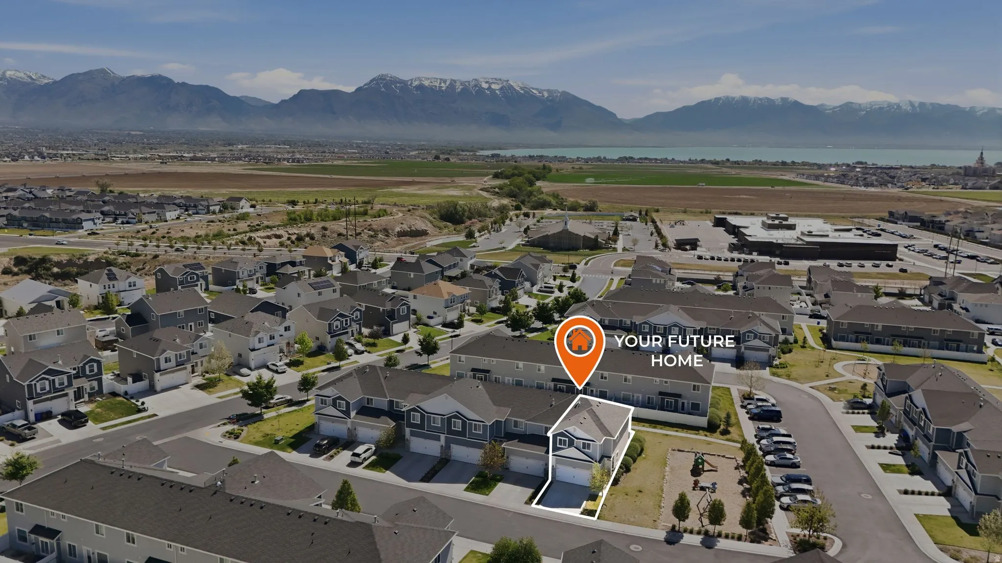 Aerial perspective showcasing a residential community with a mix of detached homes and townhomes, featuring a mountain range and a large body of water in the background