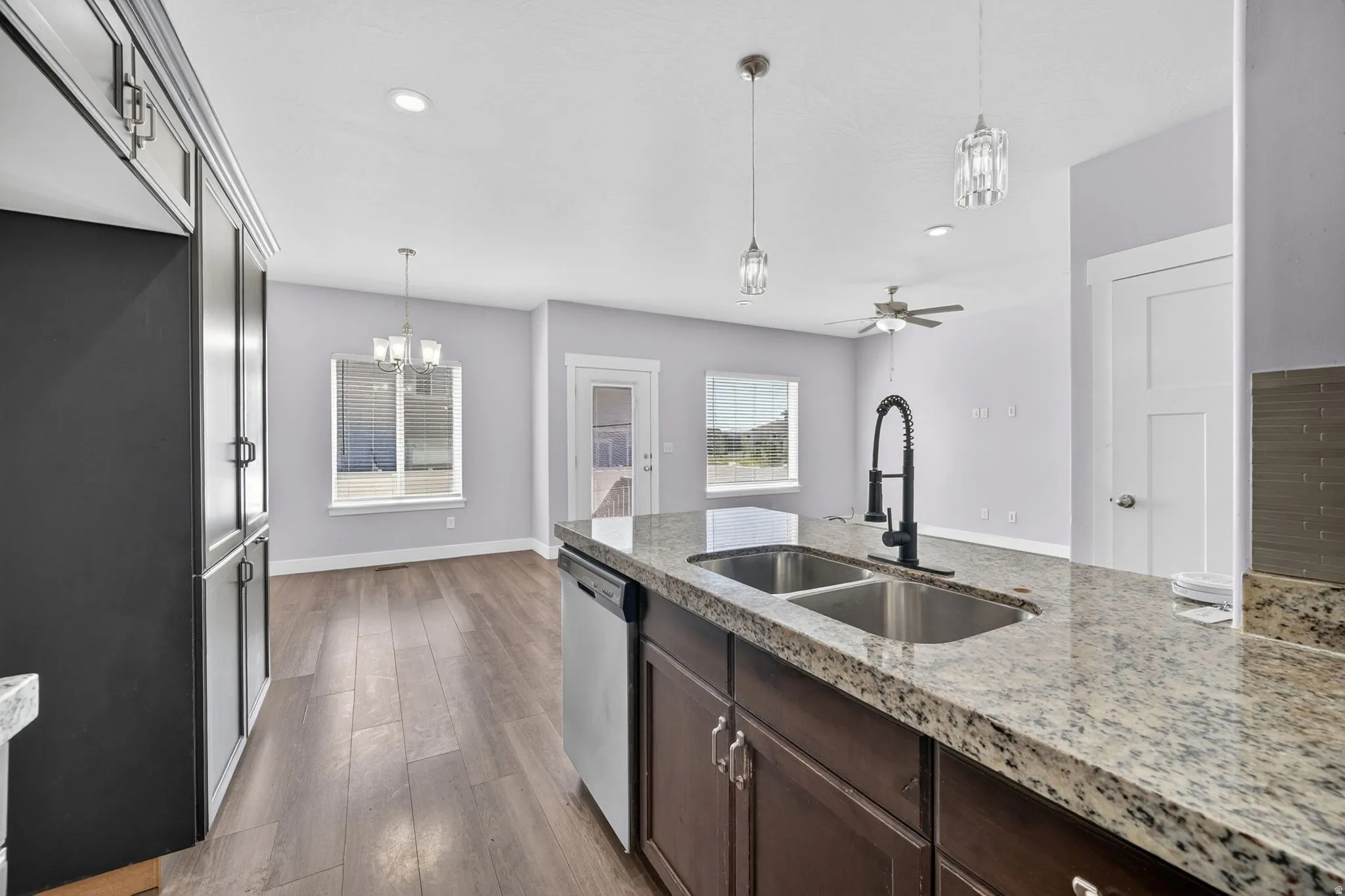 Kitchen island featuring a dual stainless steel sink and matte black faucet, granite-look countertop, and wood-finish cabinetry