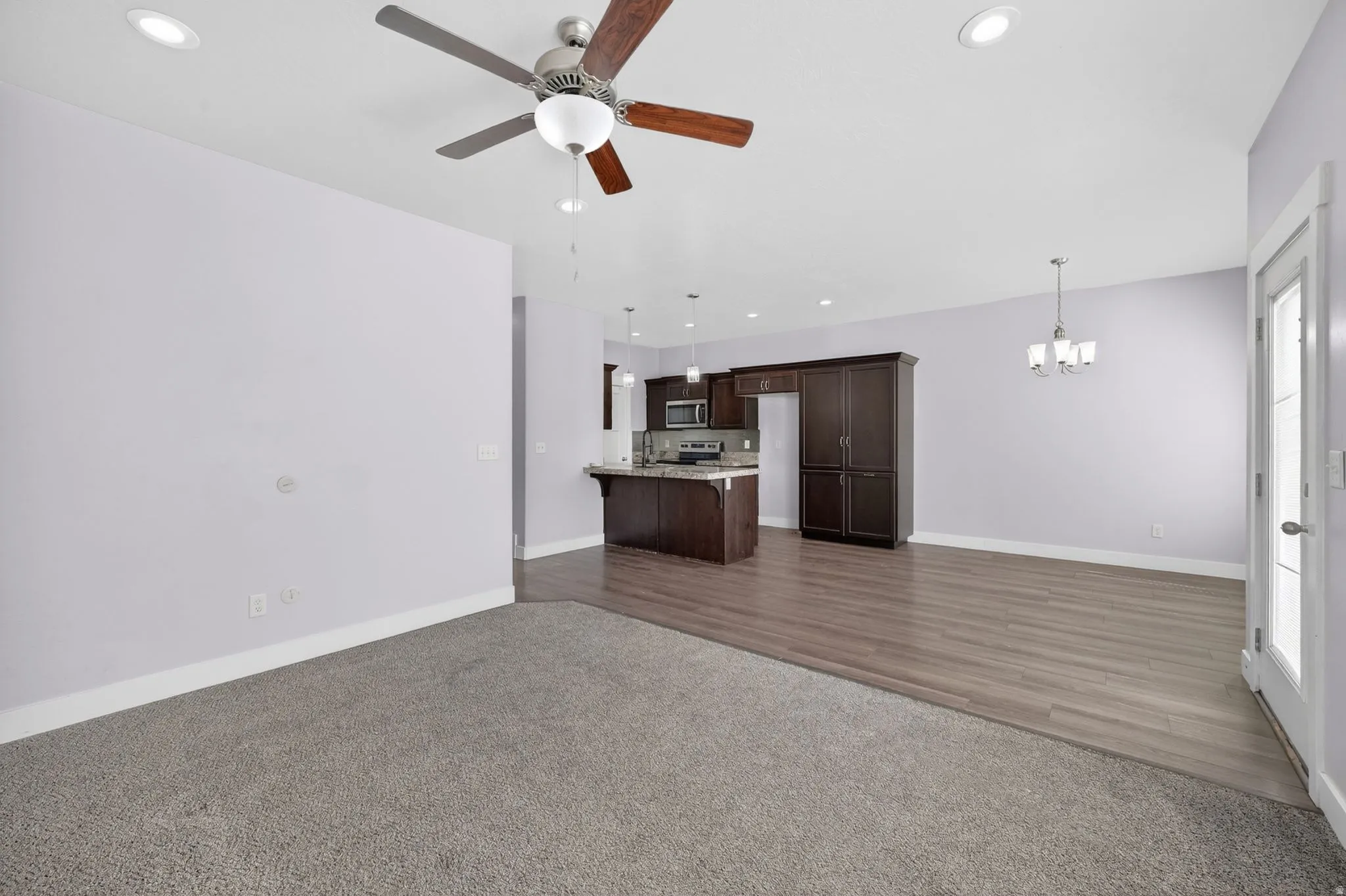 Open-concept living area featuring a ceiling fan with integrated lighting, recessed lighting, and a transition from grey carpet to wood-finish flooring