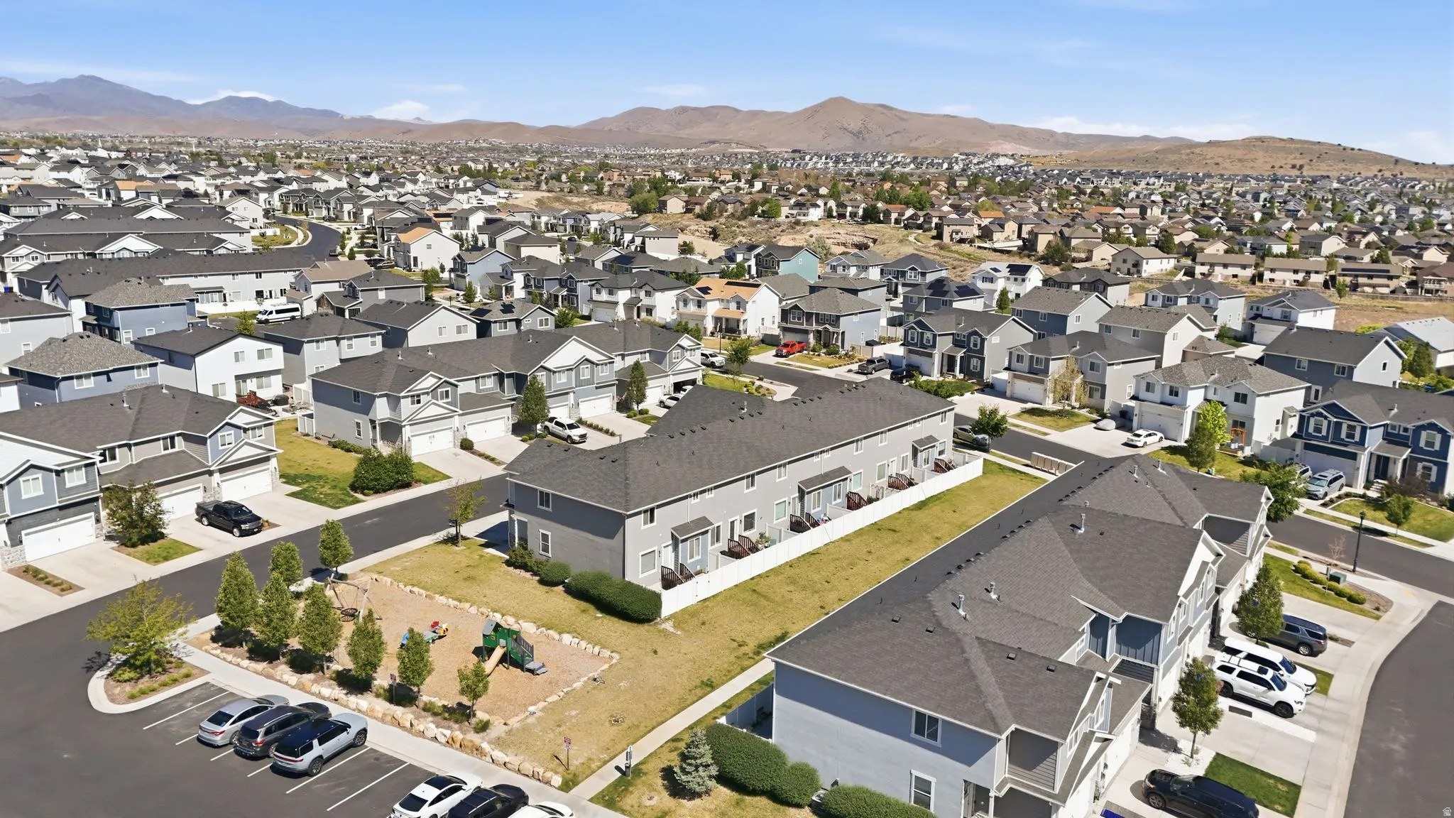 Aerial perspective of a developed residential area featuring a variety of detached homes and townhomes, paved streets, and a dedicated park area with play structures