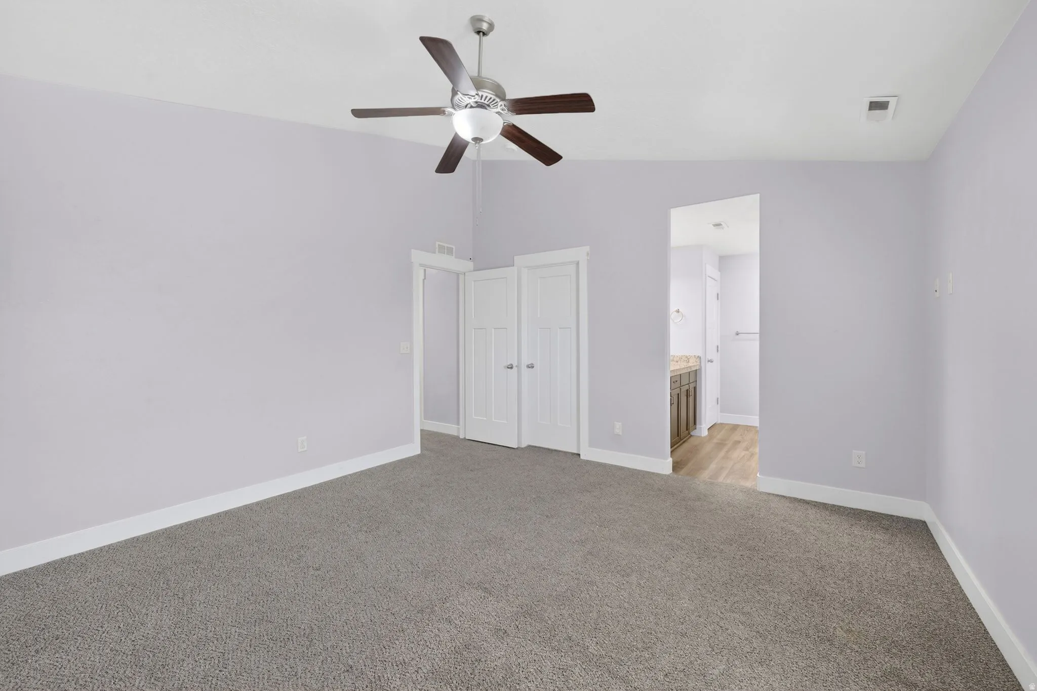 Spacious room featuring neutral carpeting, light lavender wall paint, a ceiling fan with integrated lighting, and white baseboards