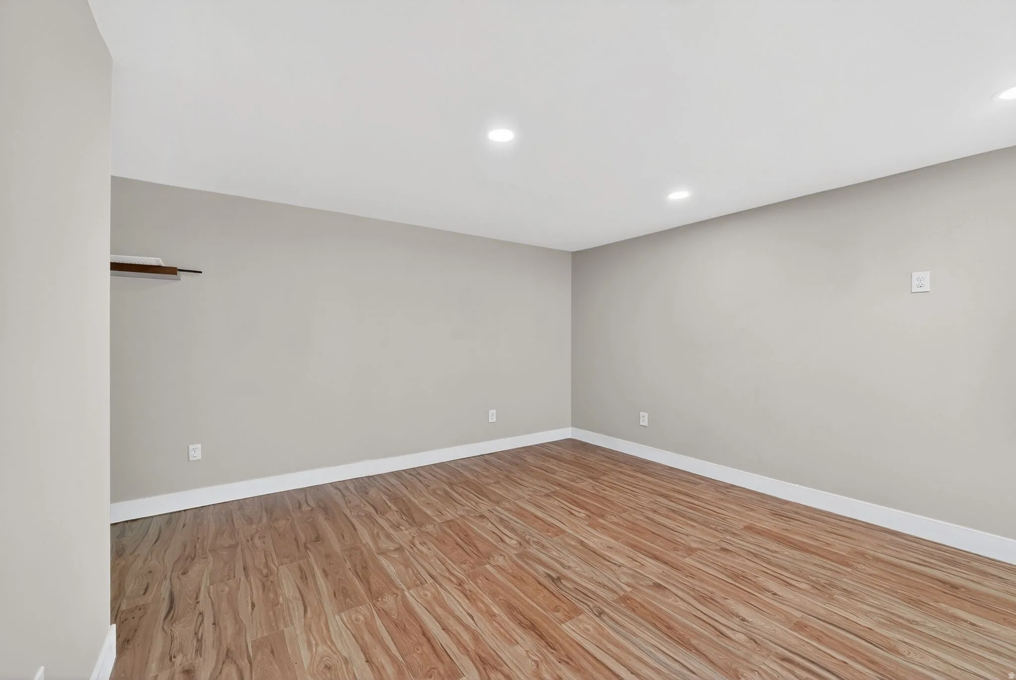 Spacious room featuring wood-finish flooring, light grey painted walls, white baseboards, and recessed ceiling lighting