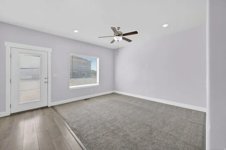 Spacious room featuring light gray walls, recessed lighting, a ceiling fan with light fixture, a window with horizontal blinds, and a glass-paneled door