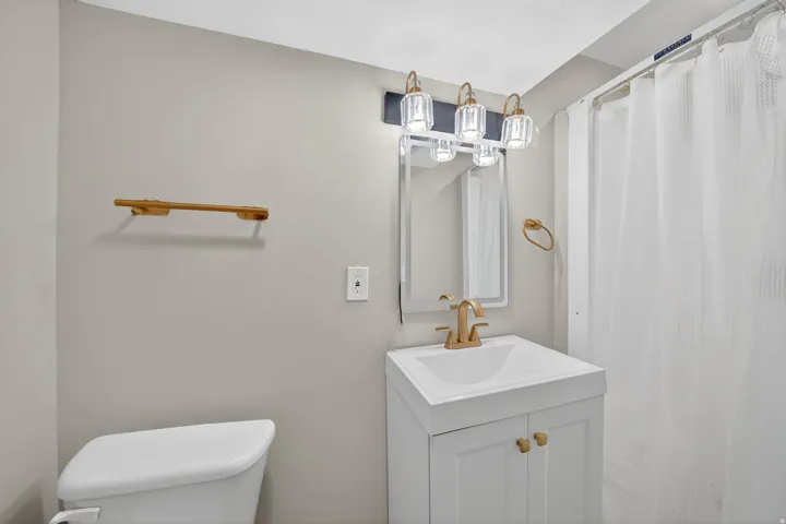 Bathroom featuring a white vanity with a single basin sink, gold-finish faucet, and coordinating gold-finish hardware