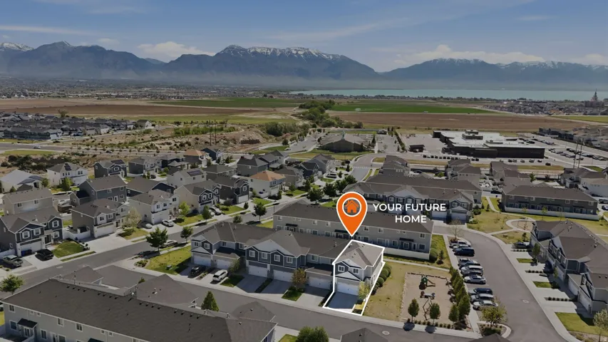 Aerial perspective showcasing a residential community with a mix of detached homes and townhomes, featuring a mountain range and a large body of water in the background
