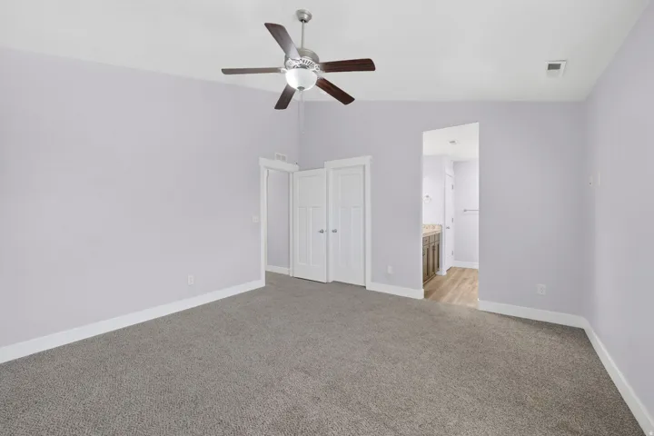 Spacious room featuring neutral carpeting, light lavender wall paint, a ceiling fan with integrated lighting, and white baseboards