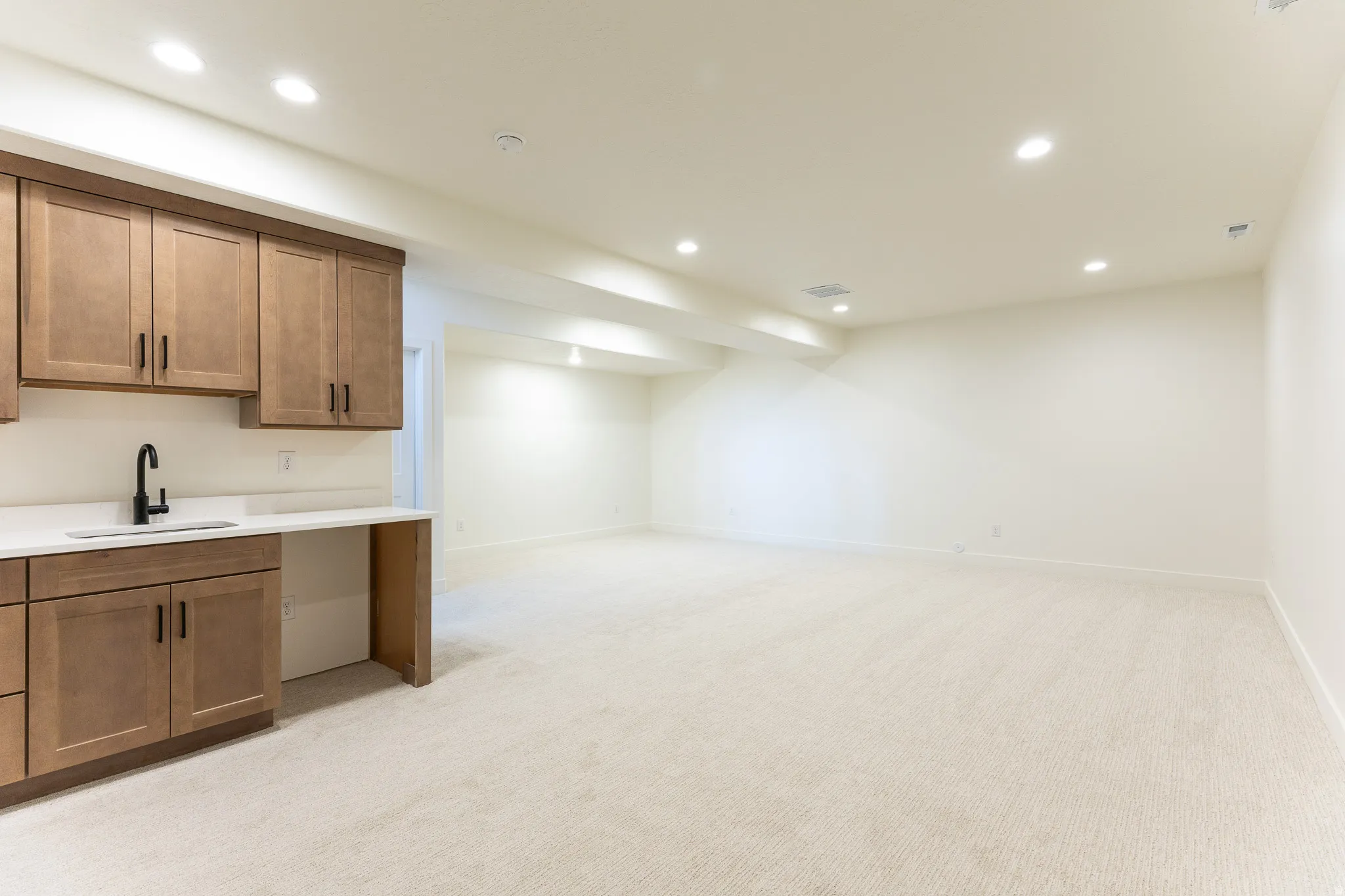 Spacious room featuring a built-in wet bar with wood-finish cabinetry, a white countertop, and a matte black faucet