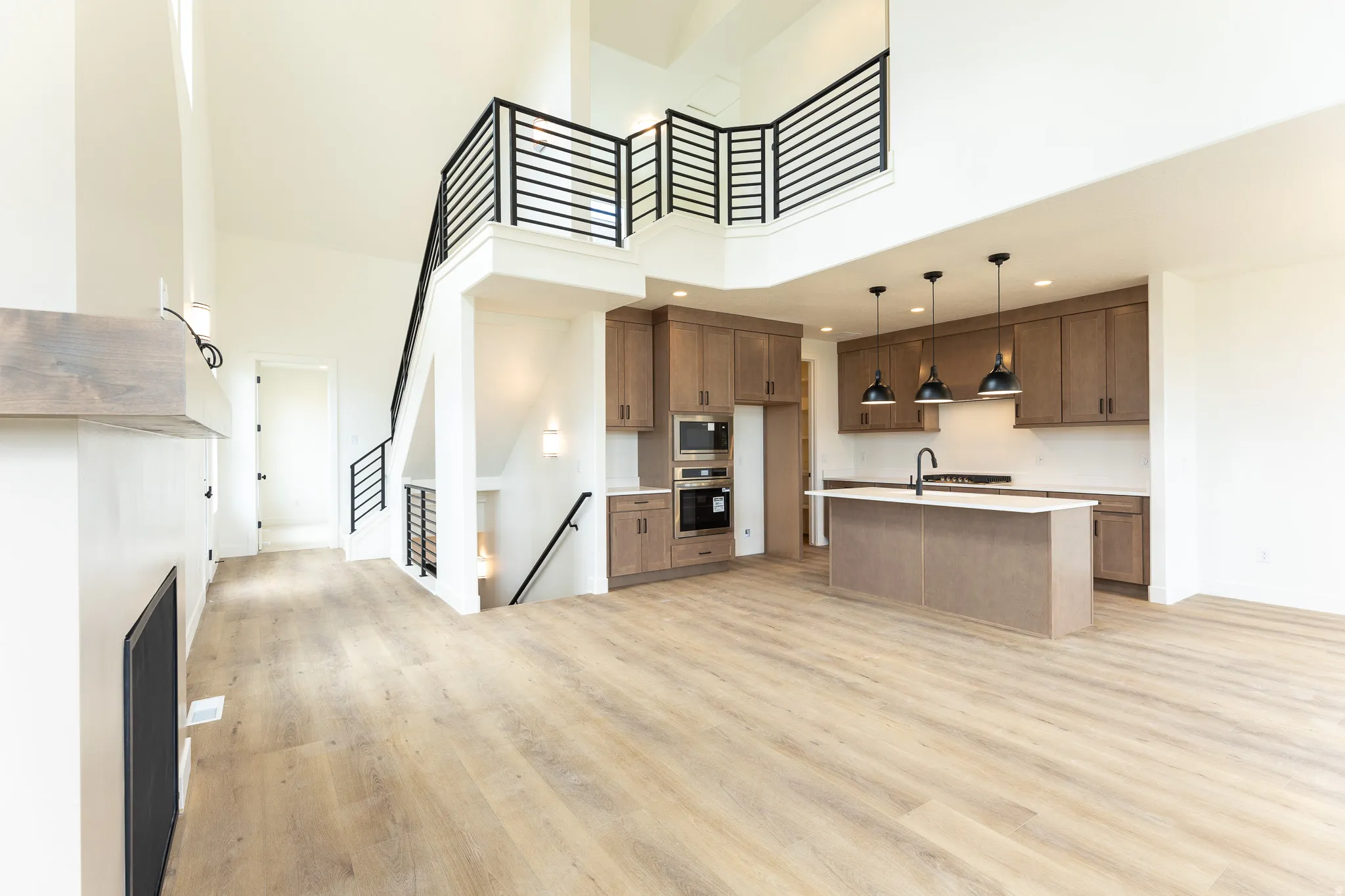 Open-concept living area featuring light wood-finish flooring, a two-story ceiling, and a prominent staircase with black metal railings