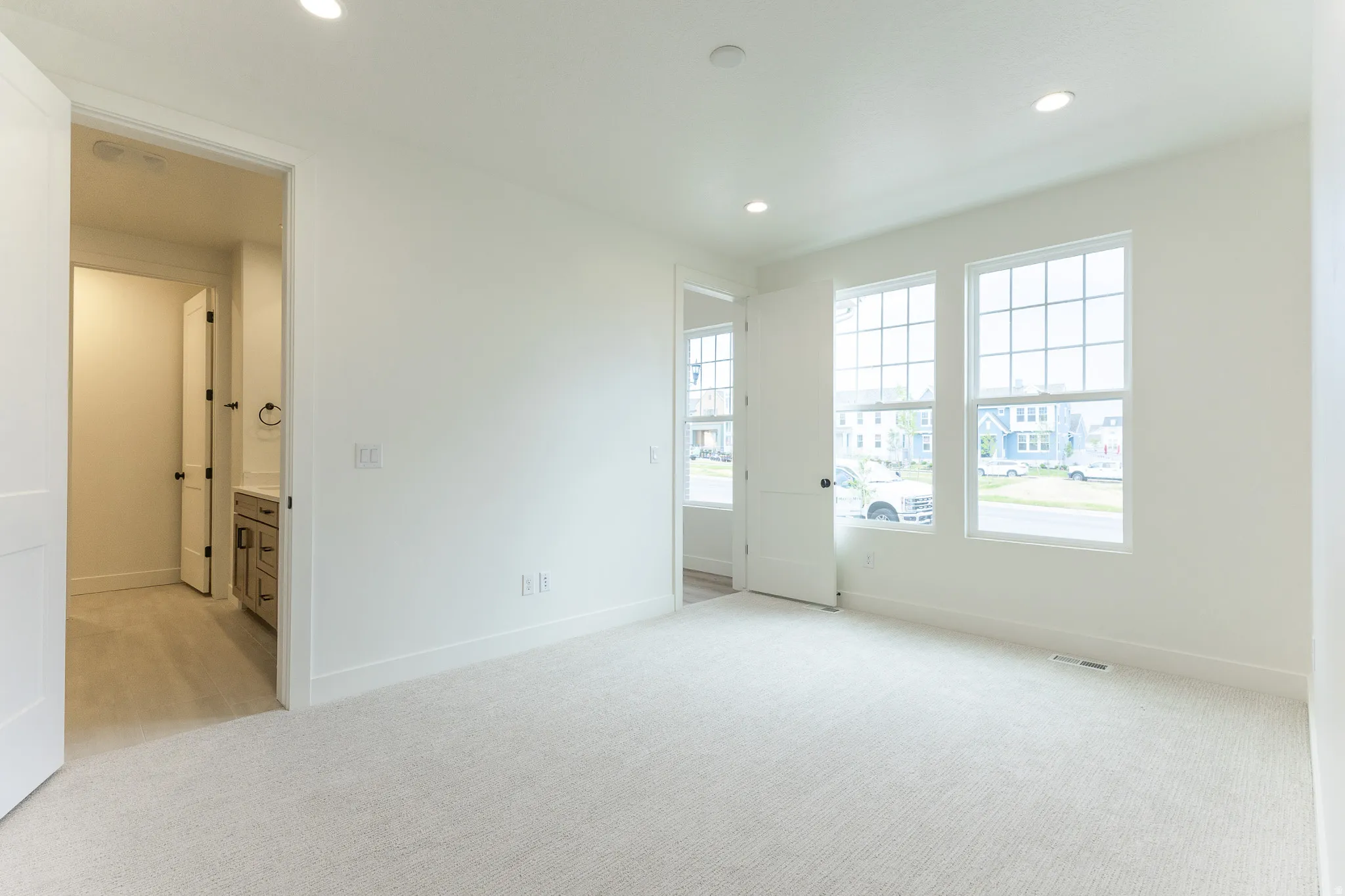 Primary bedroom on Main featuring three double-hung windows, recessed lighting, and light-toned carpeting