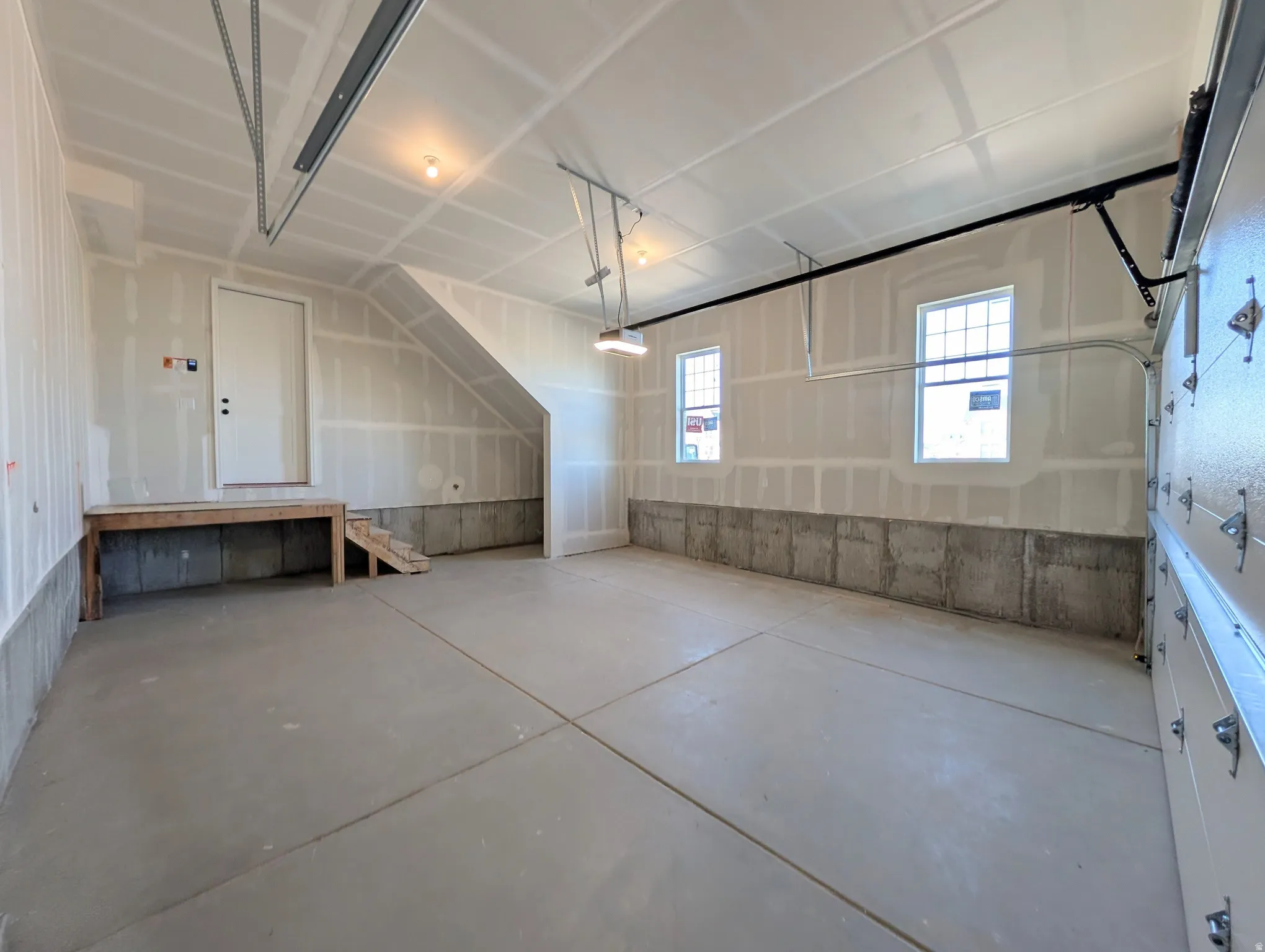 Spacious two-car garage featuring a concrete floor, exposed concrete foundation, and two window openings
