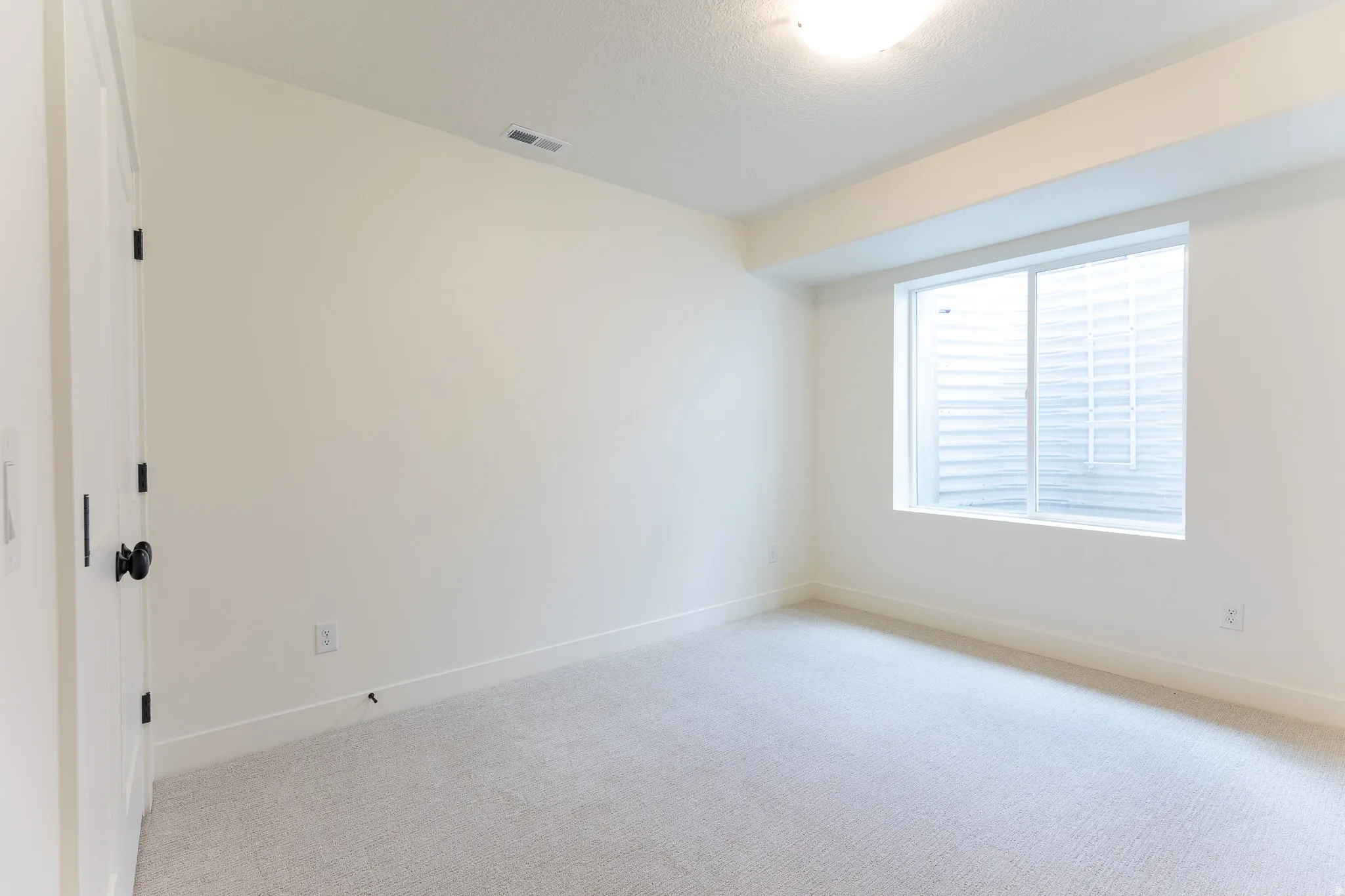 Neutral-toned room featuring a single window with white trim, light-colored carpeting, and white walls