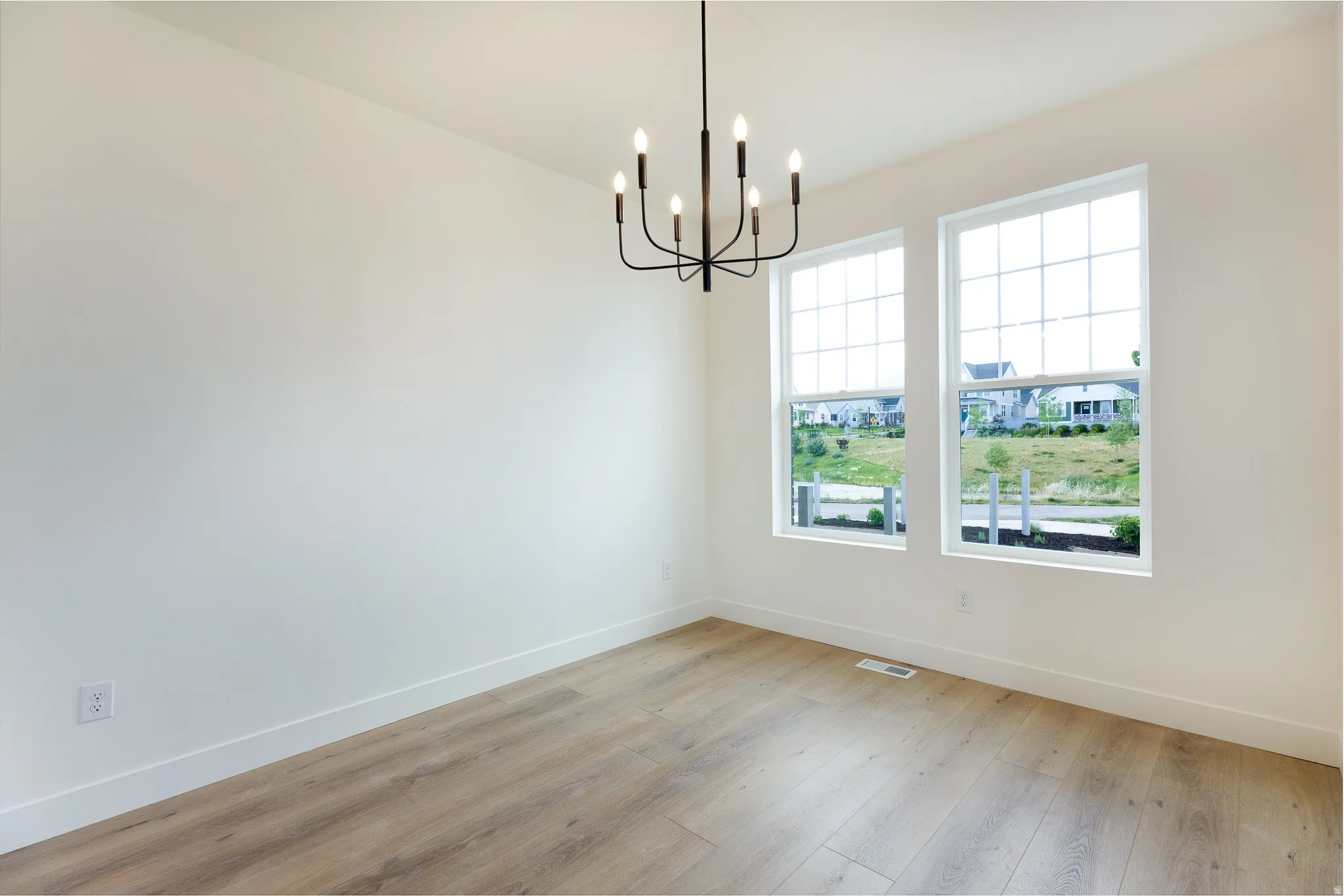 Bright interior space featuring a modern chandelier, two large windows with grid patterns, light wood-finish flooring, and white baseboards