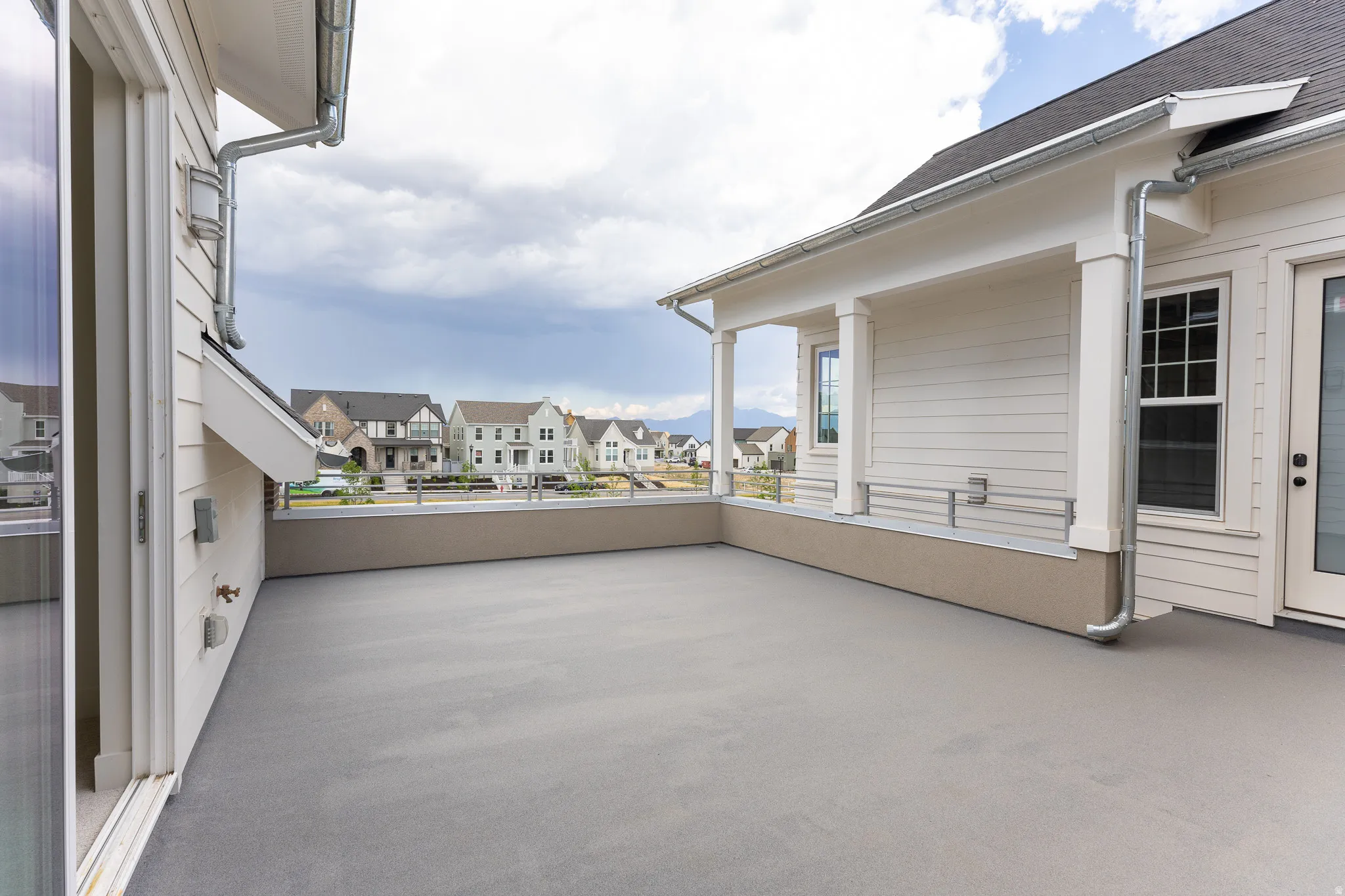 Expansive outdoor deck featuring a concrete surface, a partial covered patio area with support columns, and a glass-paneled door