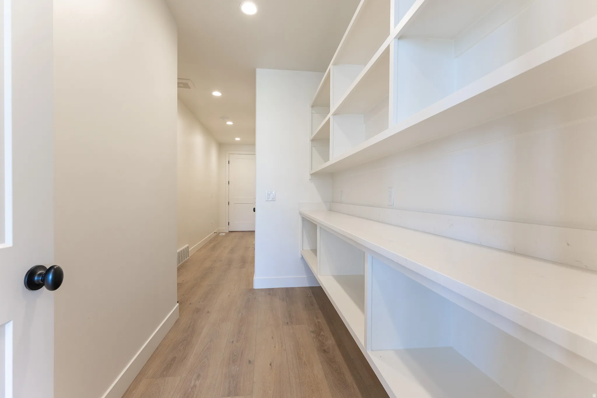 Spacious pantry featuring extensive built-in shelving, a lower countertop surface, integrated recessed lighting, and wood-finish flooring