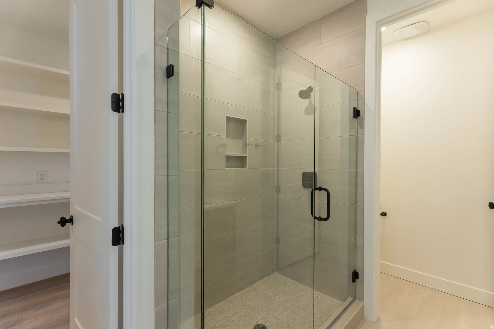 Glass-enclosed shower featuring light-toned tile walls and a built-in niche