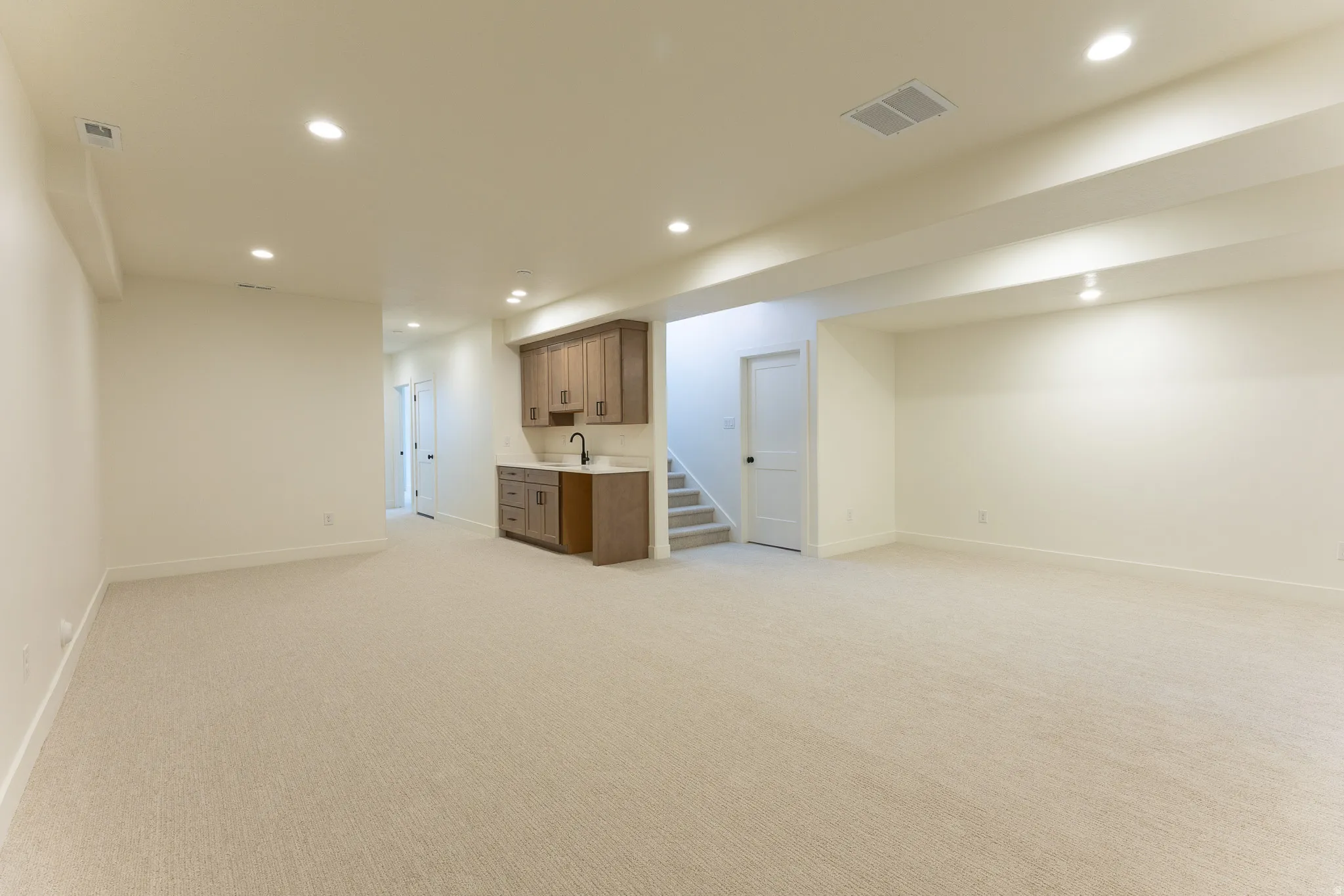 Spacious open-concept lower level featuring plush carpet flooring, recessed lighting, a built-in wet bar with wood cabinetry, a sink, and a matte black faucet