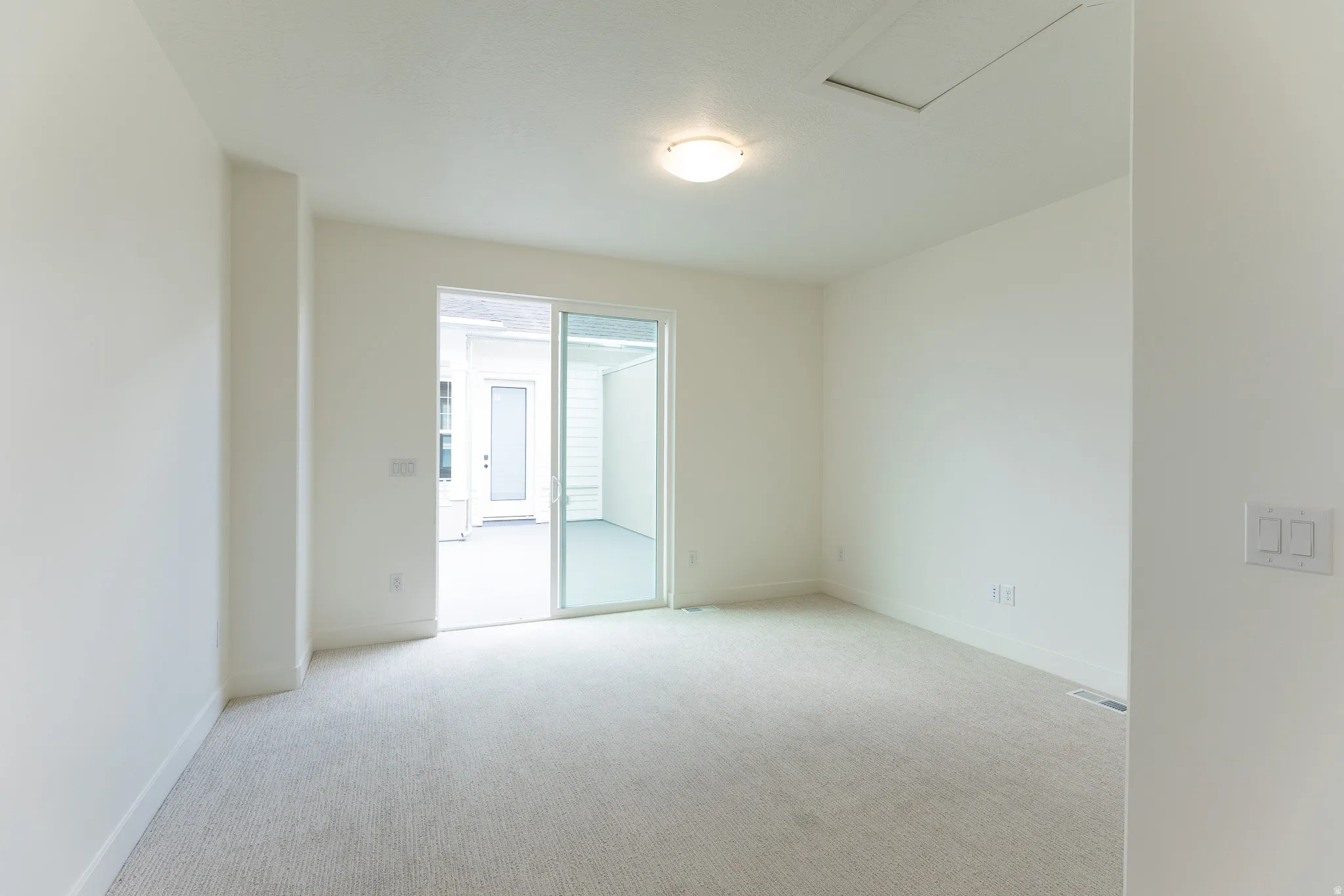 Light-colored carpeted room with white walls, featuring a sliding glass door leading to an outdoor patio