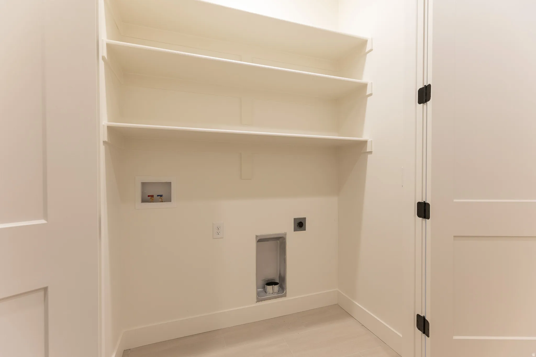 Dedicated laundry area featuring built-in shelving, appliance hookups, and light-toned flooring