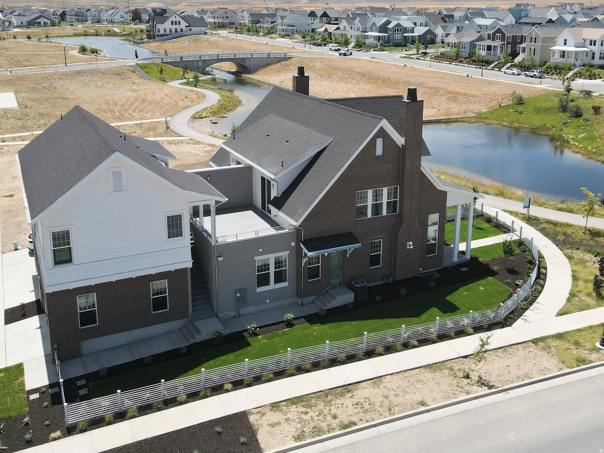 Two-story residence featuring brick and siding exteriors, a rear deck, a covered porch with pillars, and a fenced backyard with landscaped areas