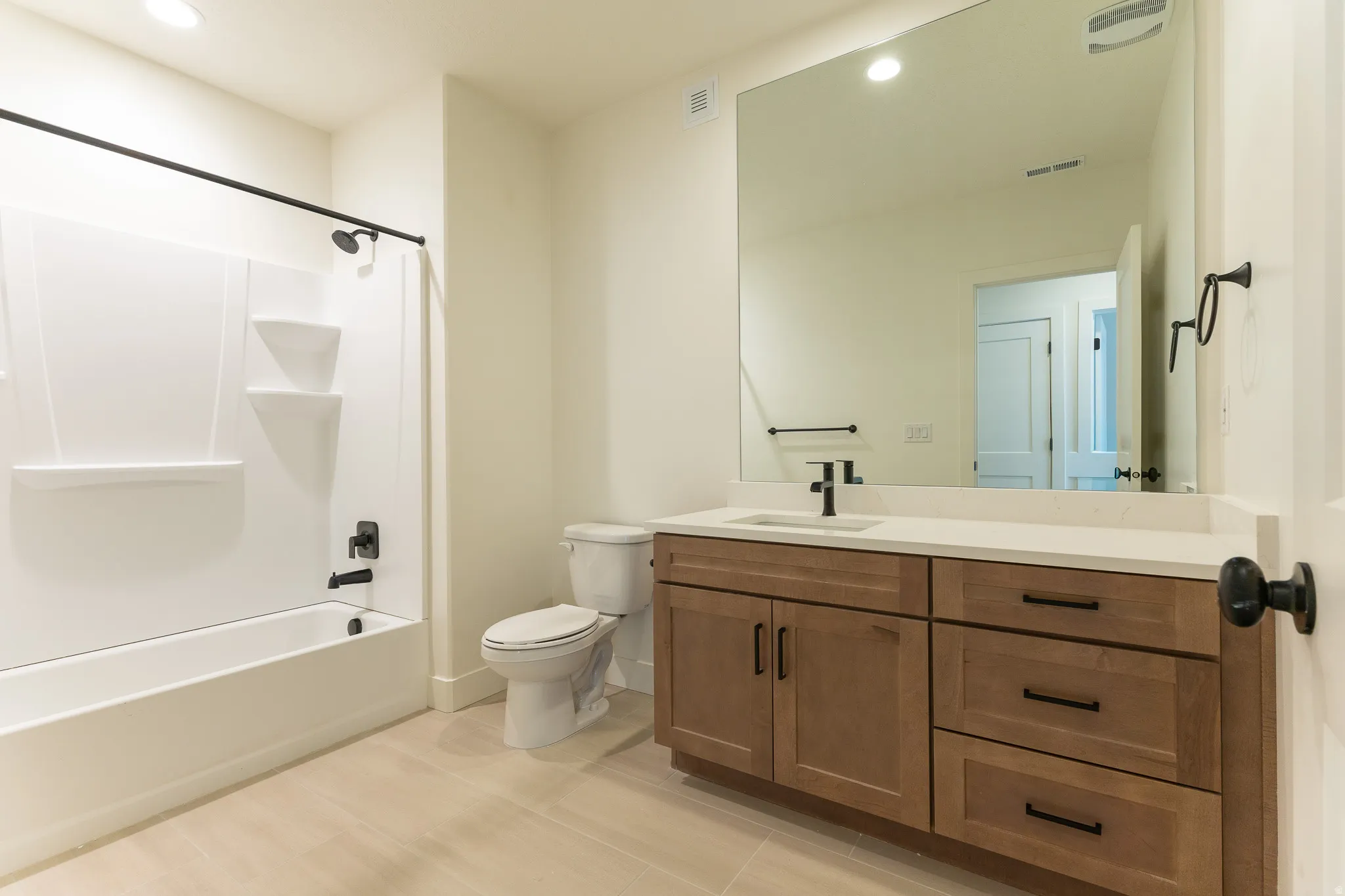 Bathroom featuring a tub and shower combination with matte black fixtures, a white vanity with an integrated sink, and an expansive mirror